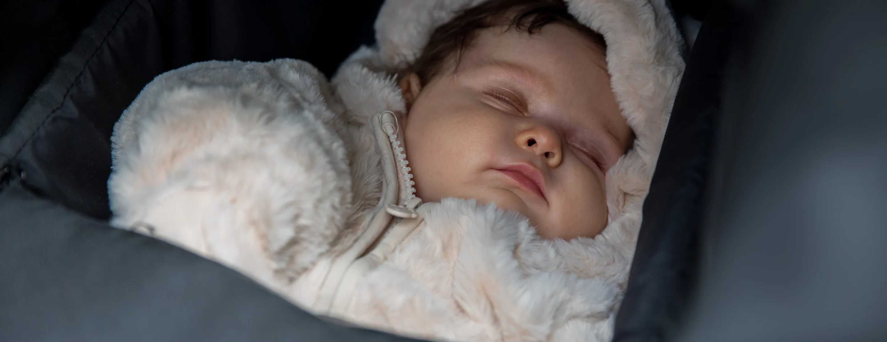 A baby asleep in a pink cot with a dummy in her mouth