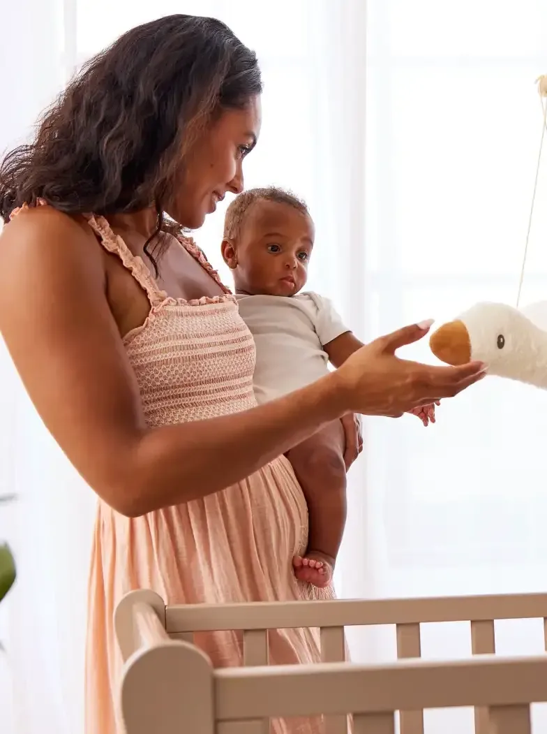Mother with baby in arms overlooking cot