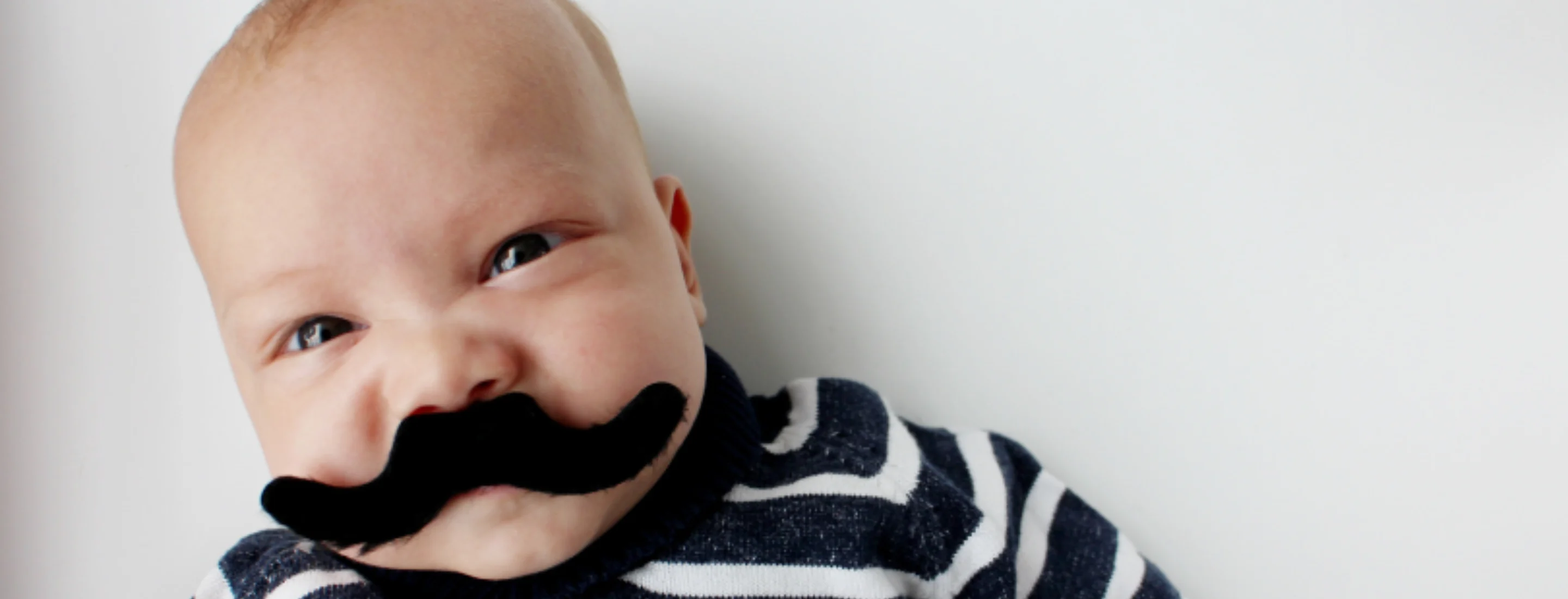 A baby wearing a fake moustache and a stripey jumper