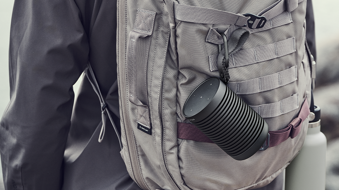 Beosound Explore Black Anthracite hanging with a carabiner from a hiker's backpack