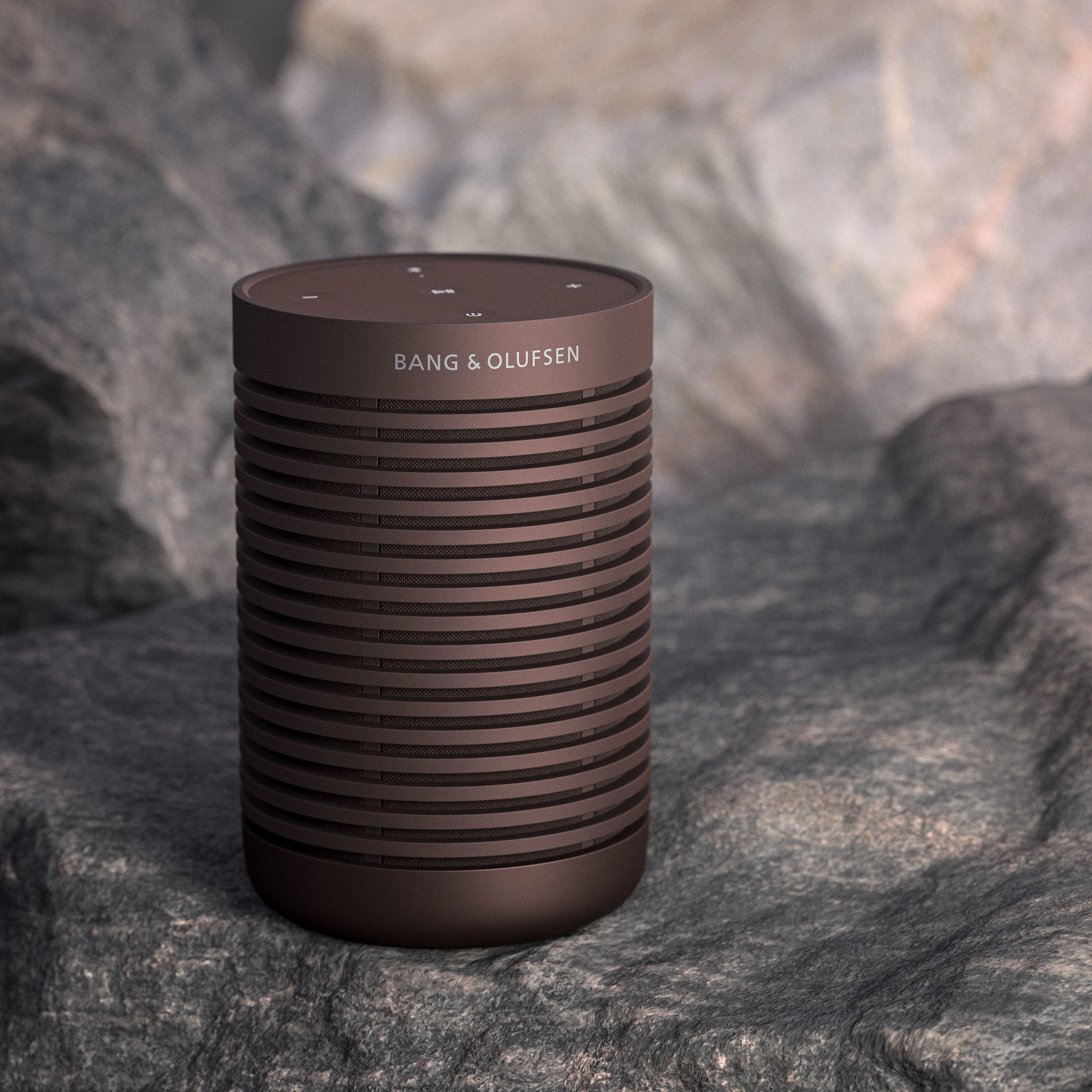 Image of the Beosound Explore portable speaker in the colour Chestnut on a rock