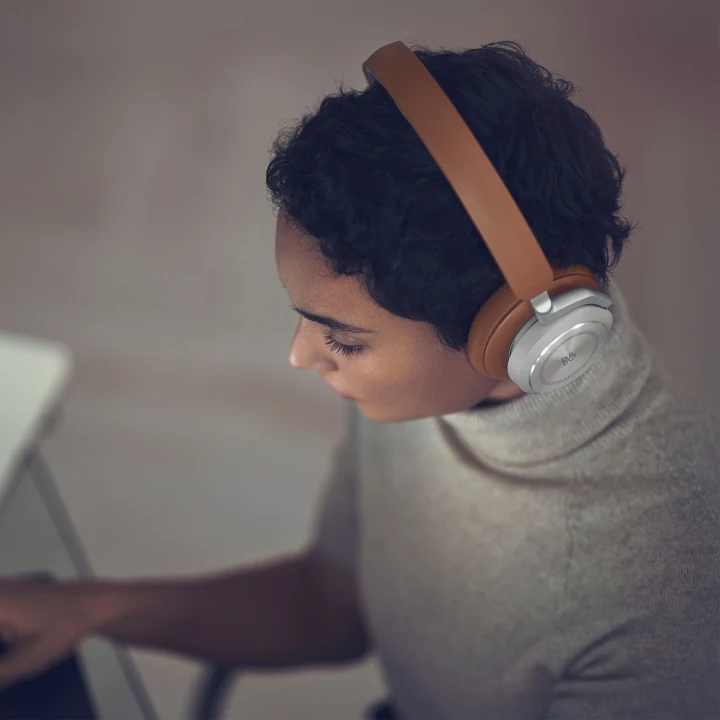 The headphones Beoplay HX Timber worn by woman working on a computer