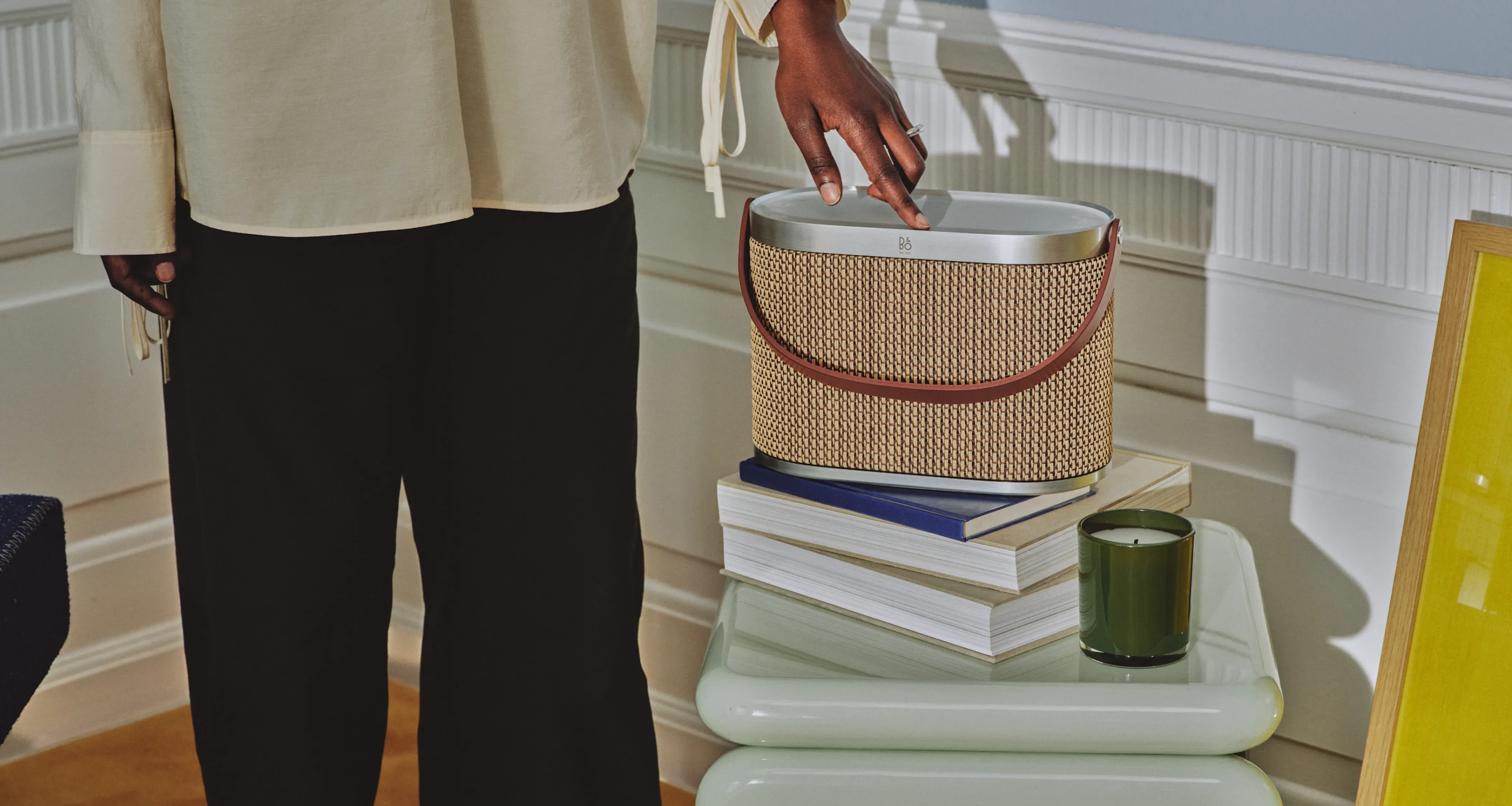 Woman using Beosound A5 in the variant Century Weave. The speaker is on a side table with books and candle.