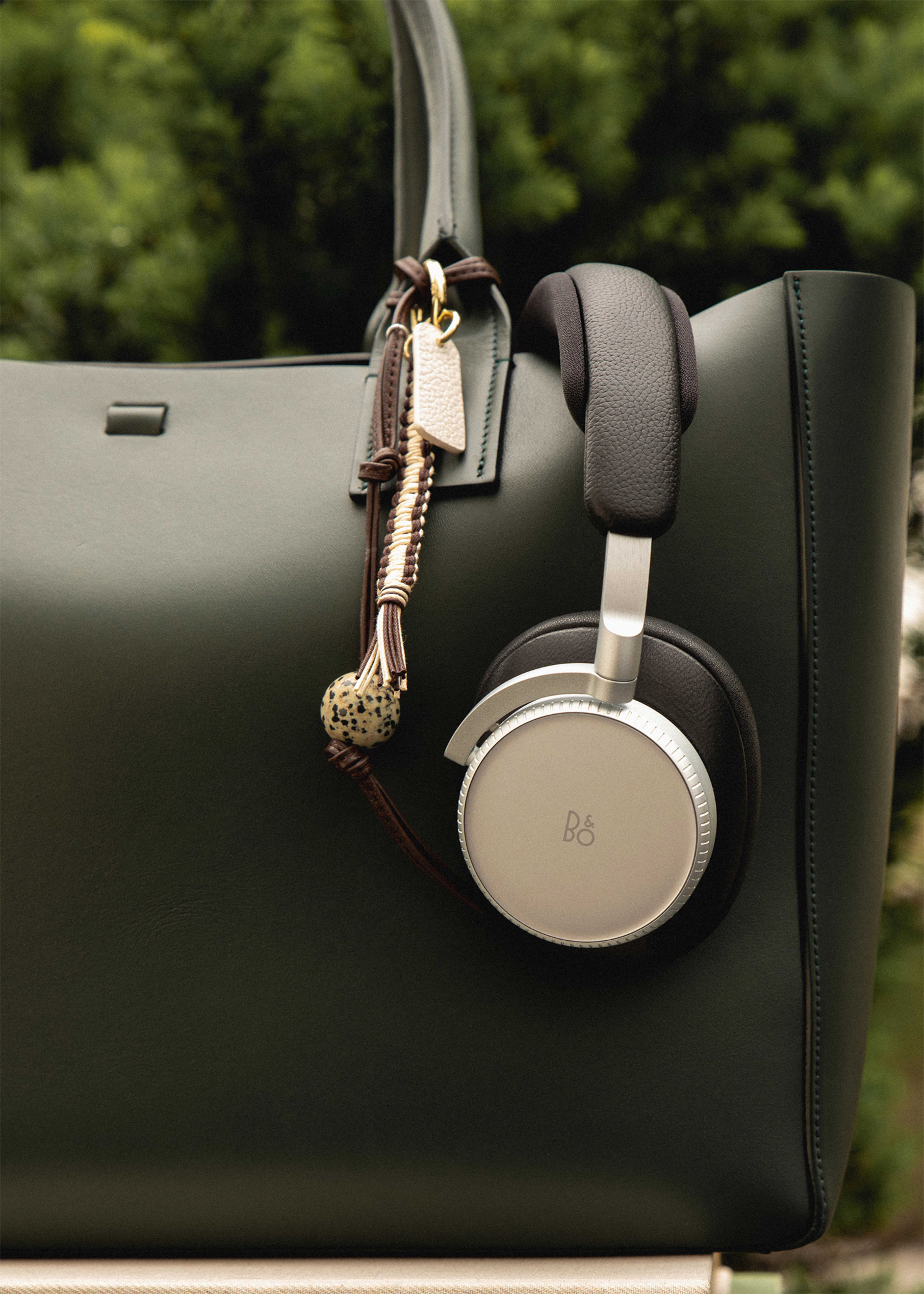 Beoplay H100 in black hanging on a leather green bag