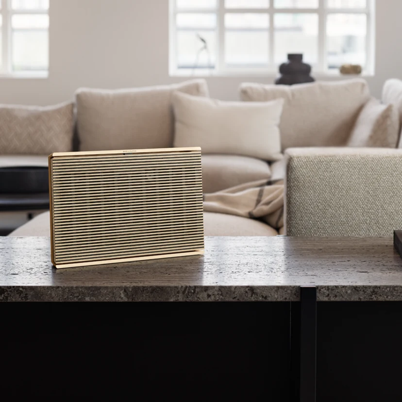 Beosound Level Gold Tone - Light Oak placed upright on a marble table in a living room