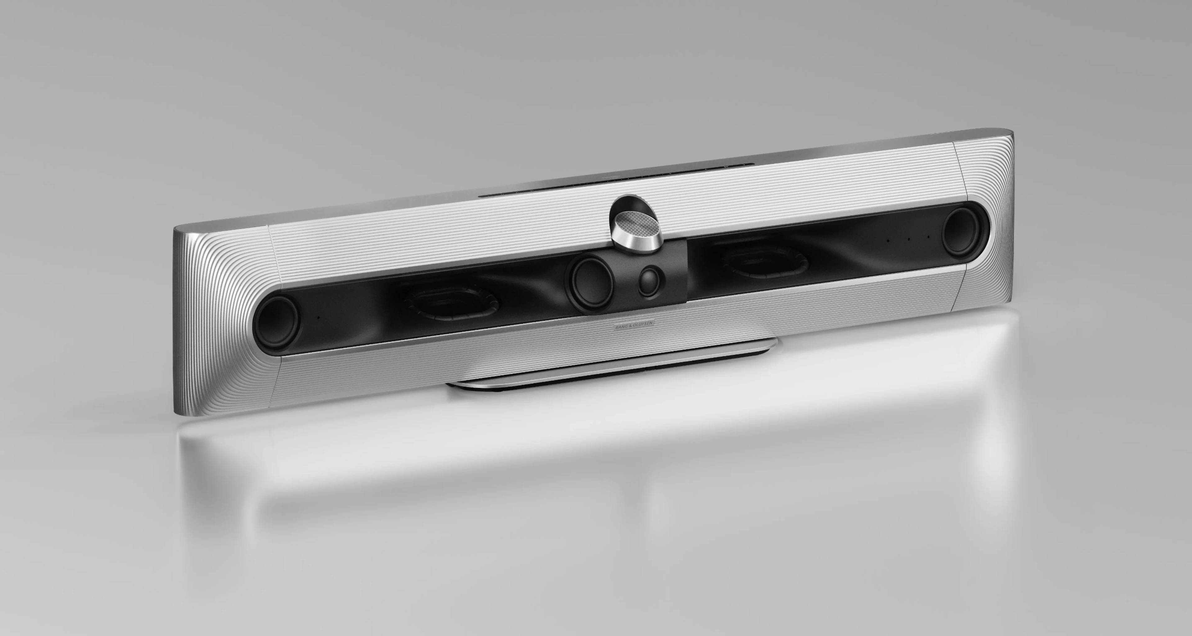 Sleek silver Beosound Premiere Haute soundbar with black speaker panel and central control dial on a white surface against gray background.