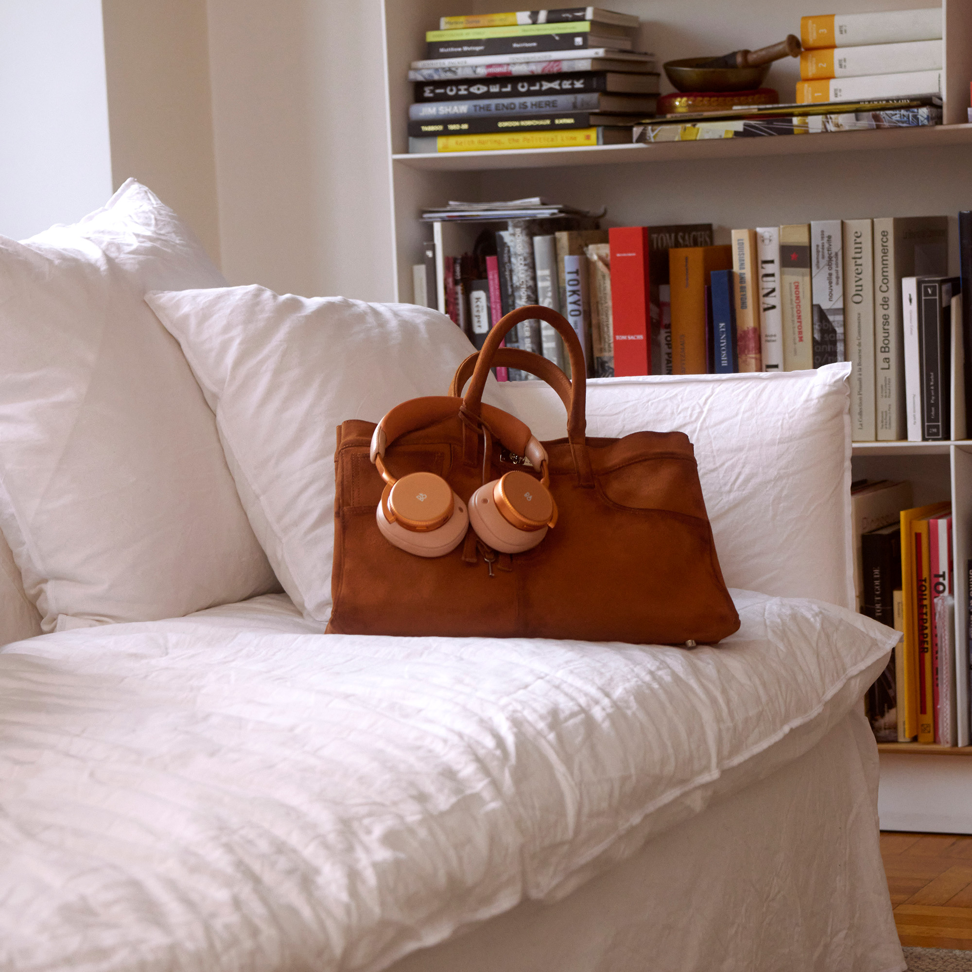 Beoplay H100 in sunset orange on a white couch and leather bag