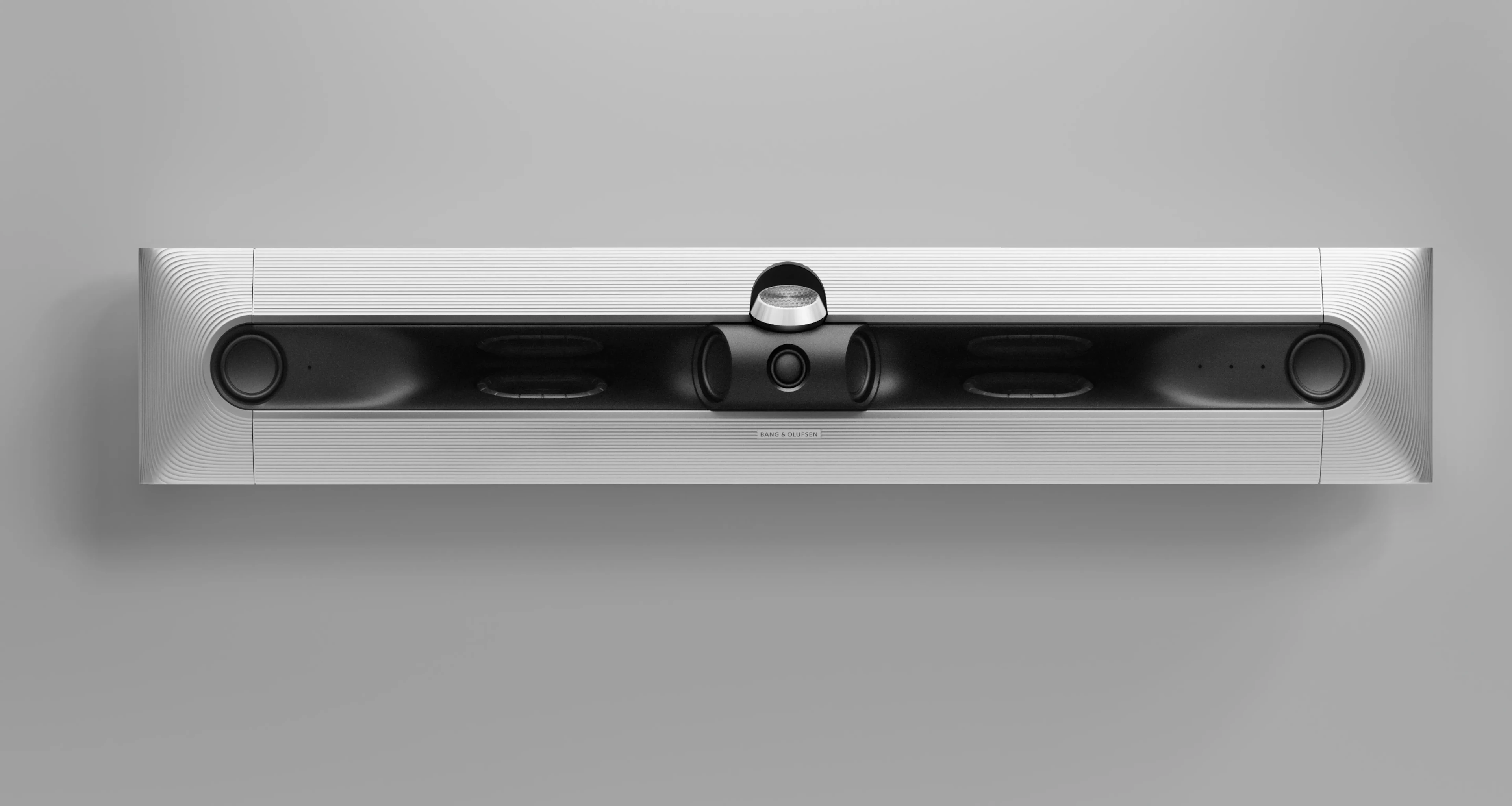 Sleek Bang & Olufsen soundbar with silver aluminum frame and black speaker grille mounted on a light gray wall.