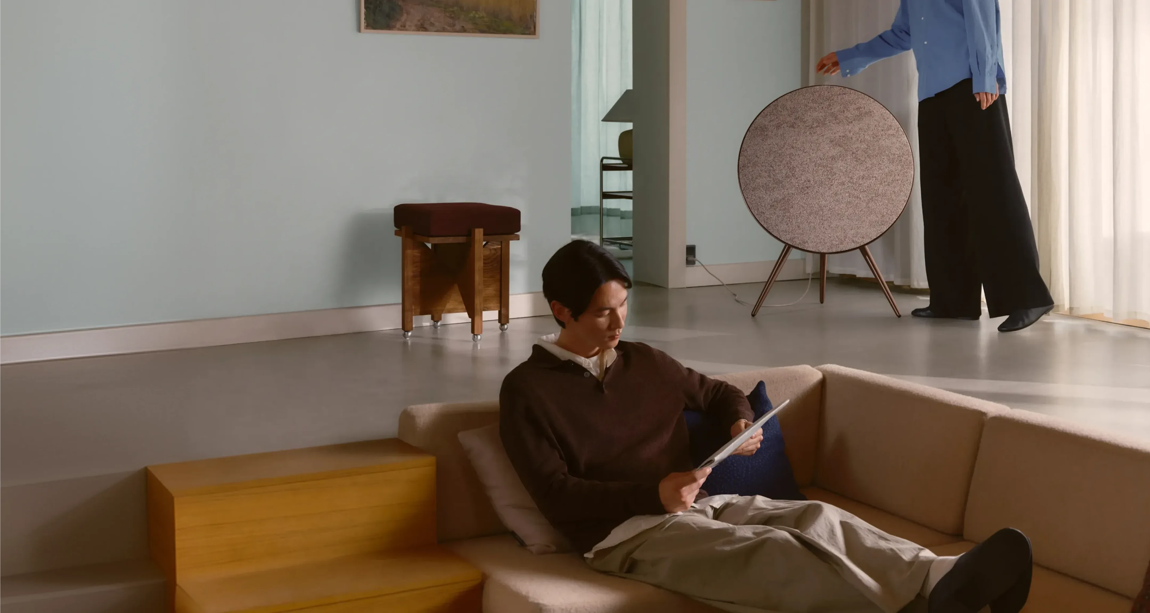 Bang & Olufsen Beosound A9 in Sienna Brown standing in a contemporary living space while a person relaxes on a sofa nearby.