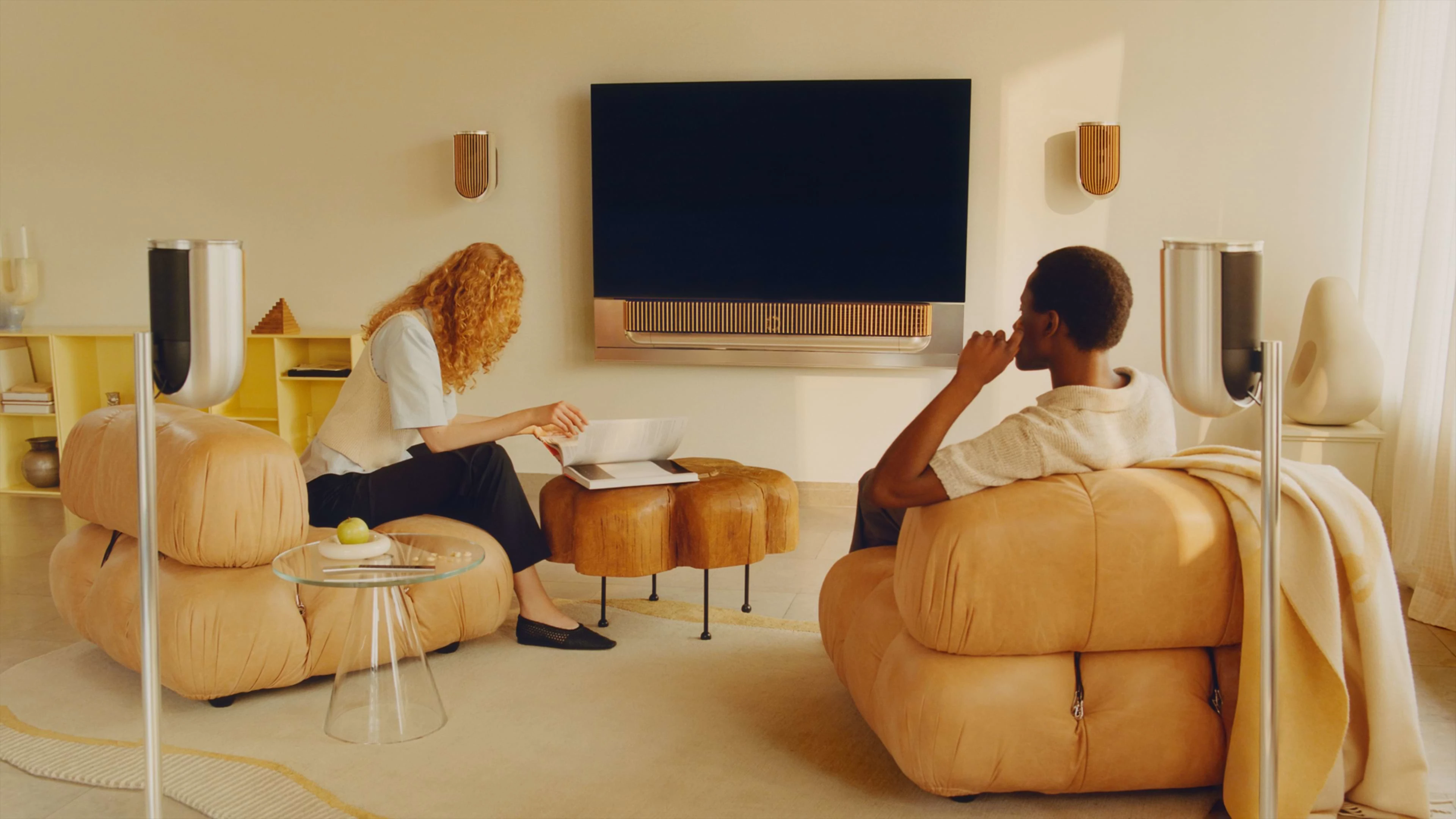 Two people sitting in a living room surrounded by B&O products