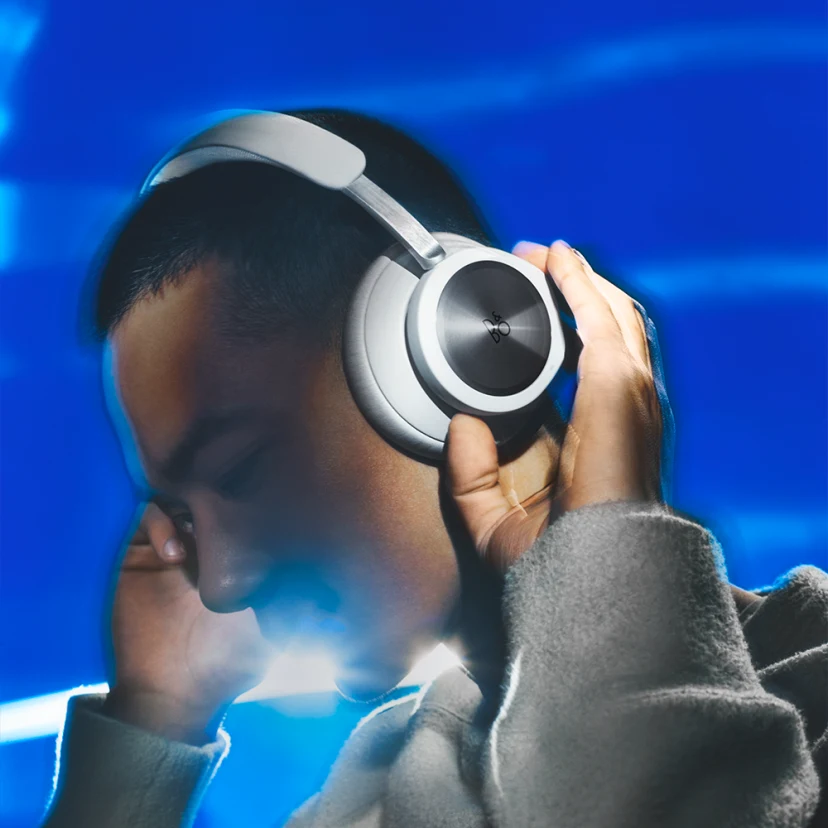 A guy smiles while wearing and listening to Beoplay Portal in Grey Mist