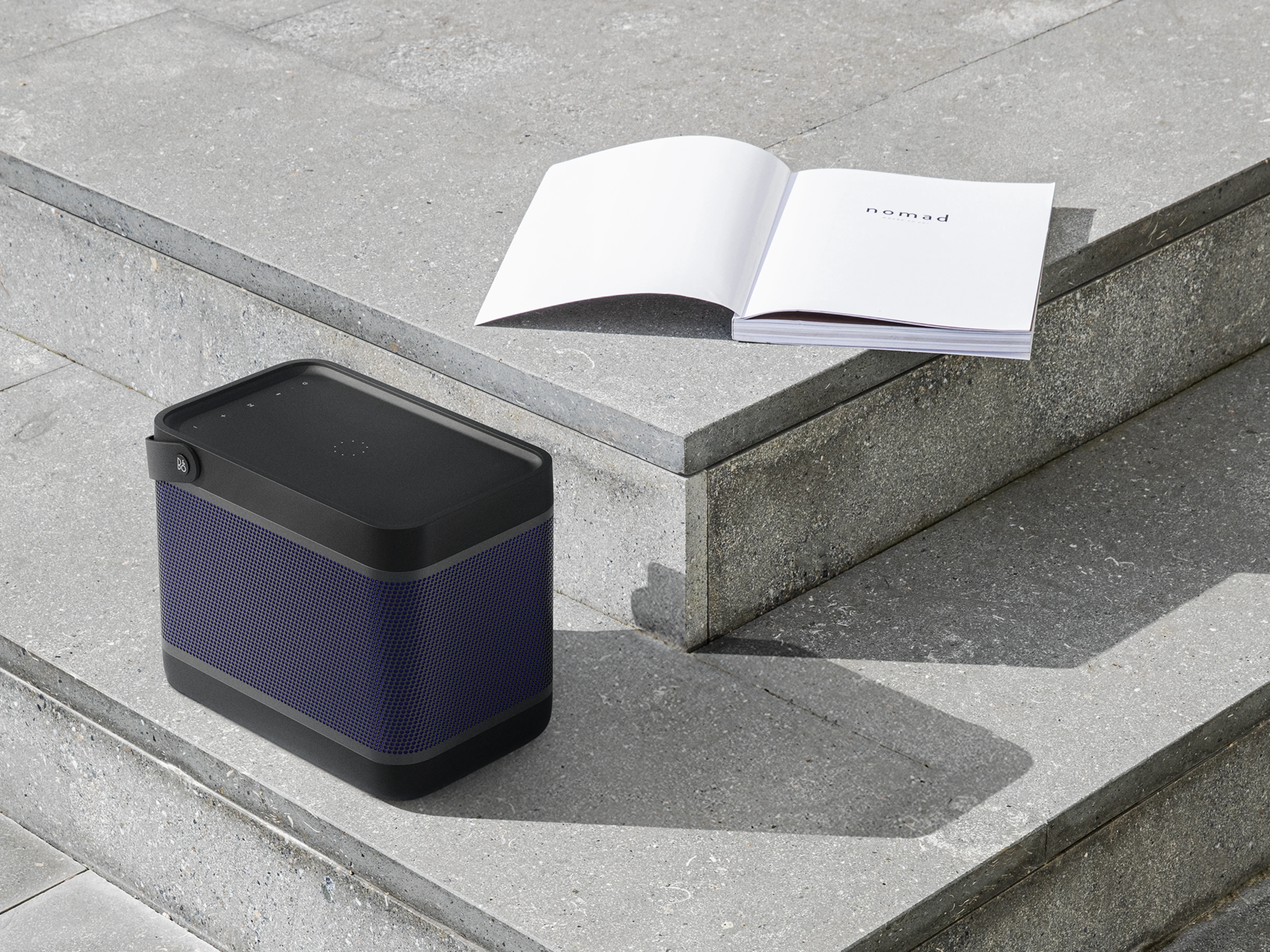 Beolit 20 displayed on concrete stairs next to an open book