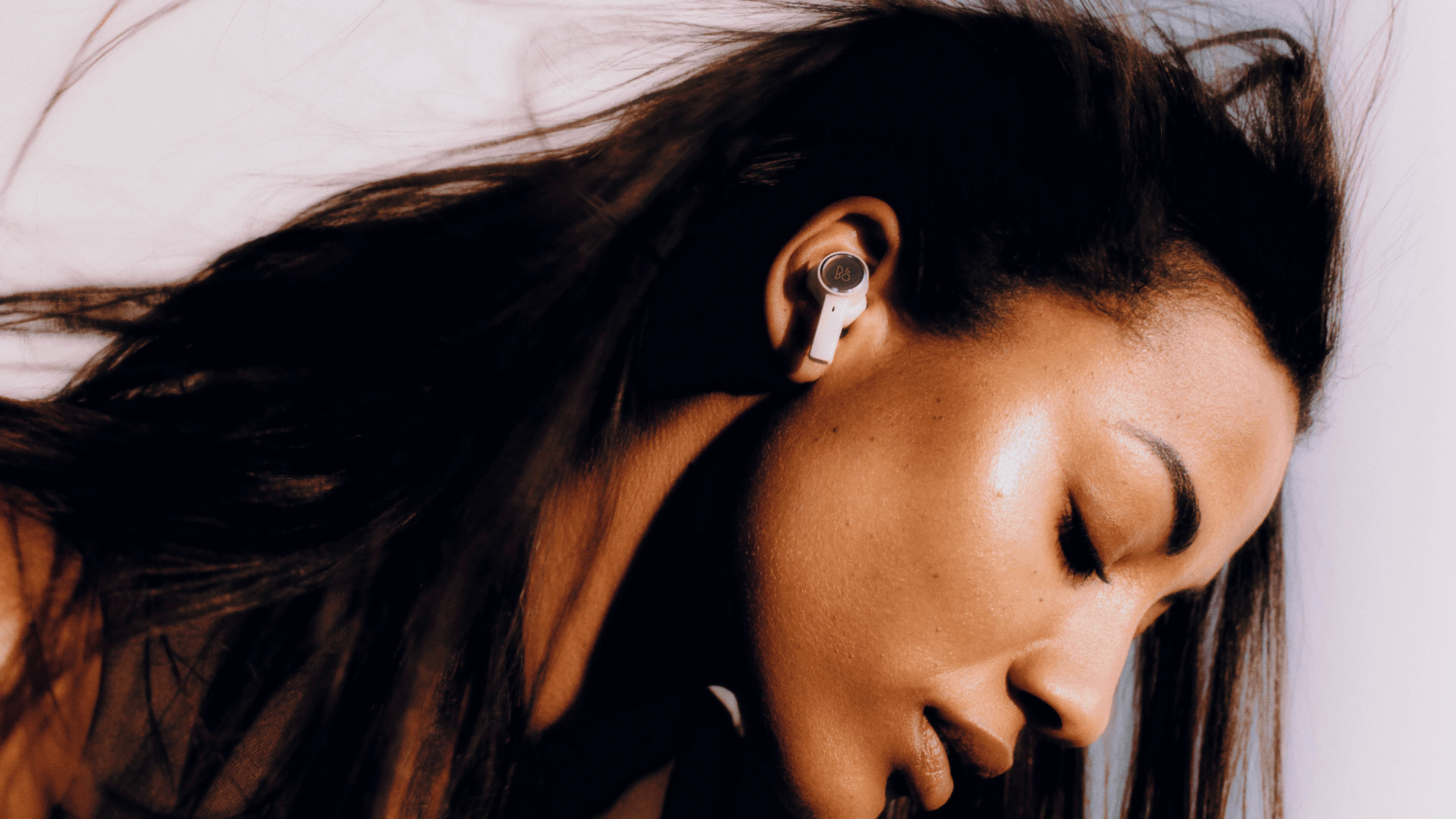 A lady listening to music with her eyes closed with gold tone Beoplay EX wireless earbuds