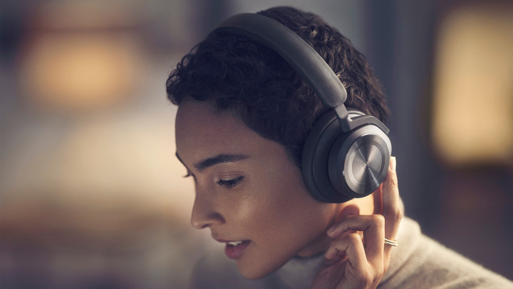 A woman using the right earcup's buttons to turn on the headphones Beoplay HX