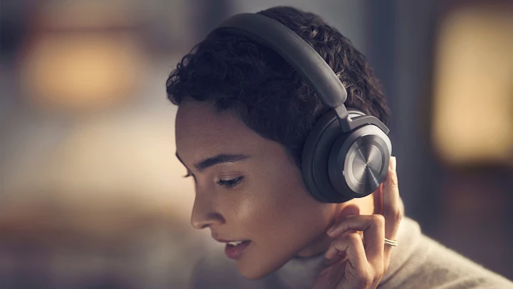 A woman using the right earcup's buttons to turn on the headphones Beoplay HX