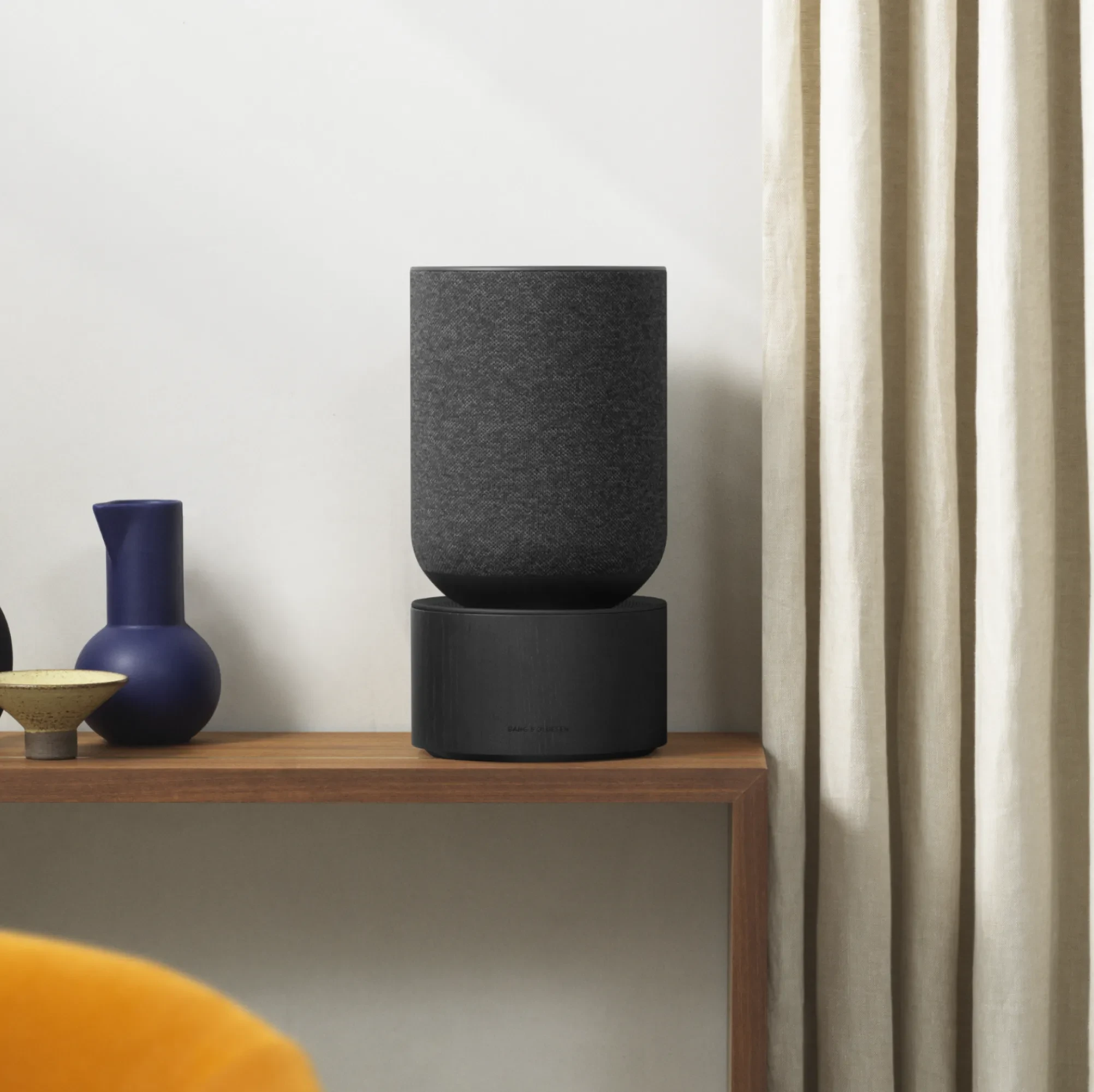 Beosound Balance black oak standing on the table next to the curtain