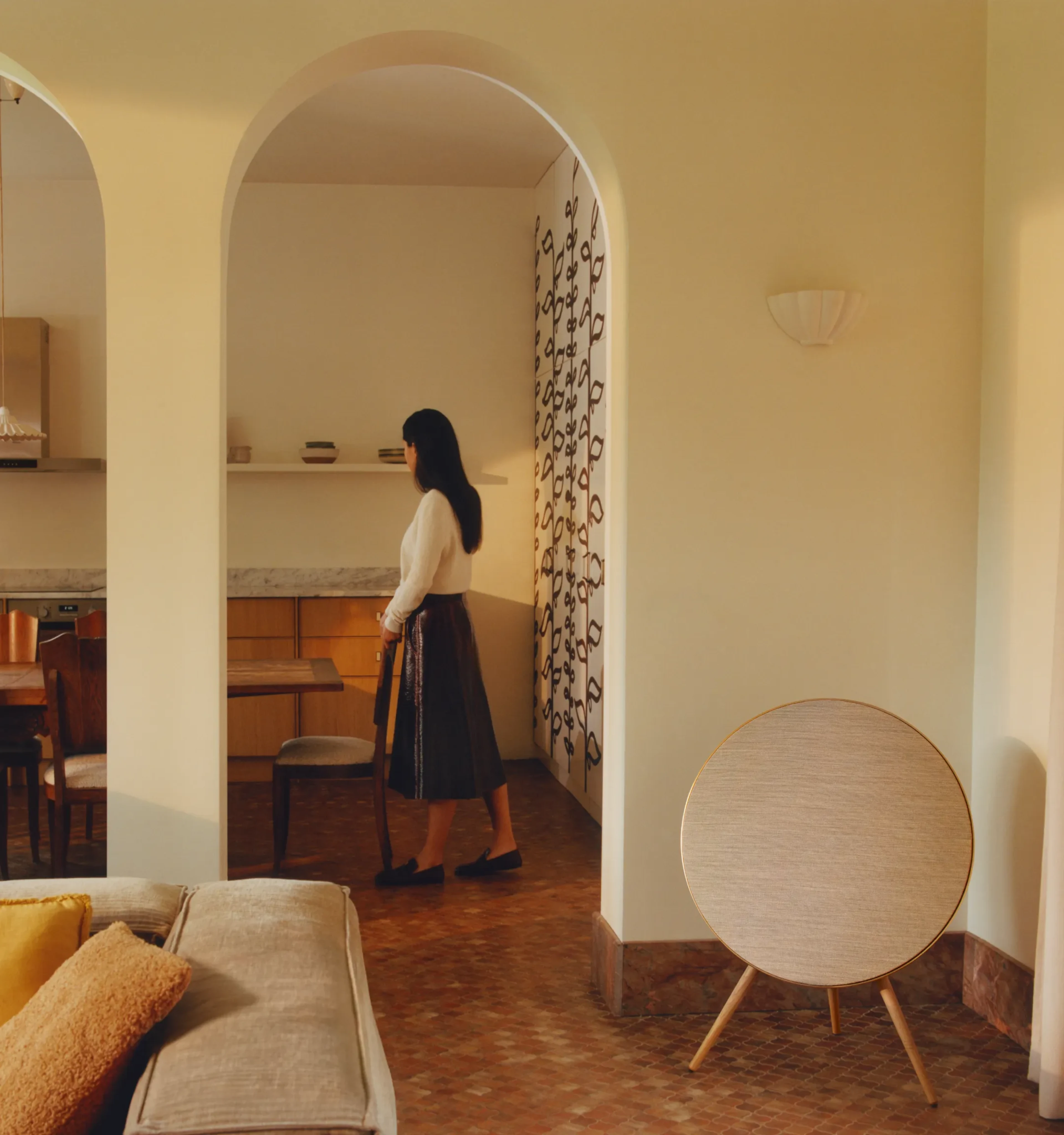 A woman standing in a dining room with Beosound A9 standing next to her