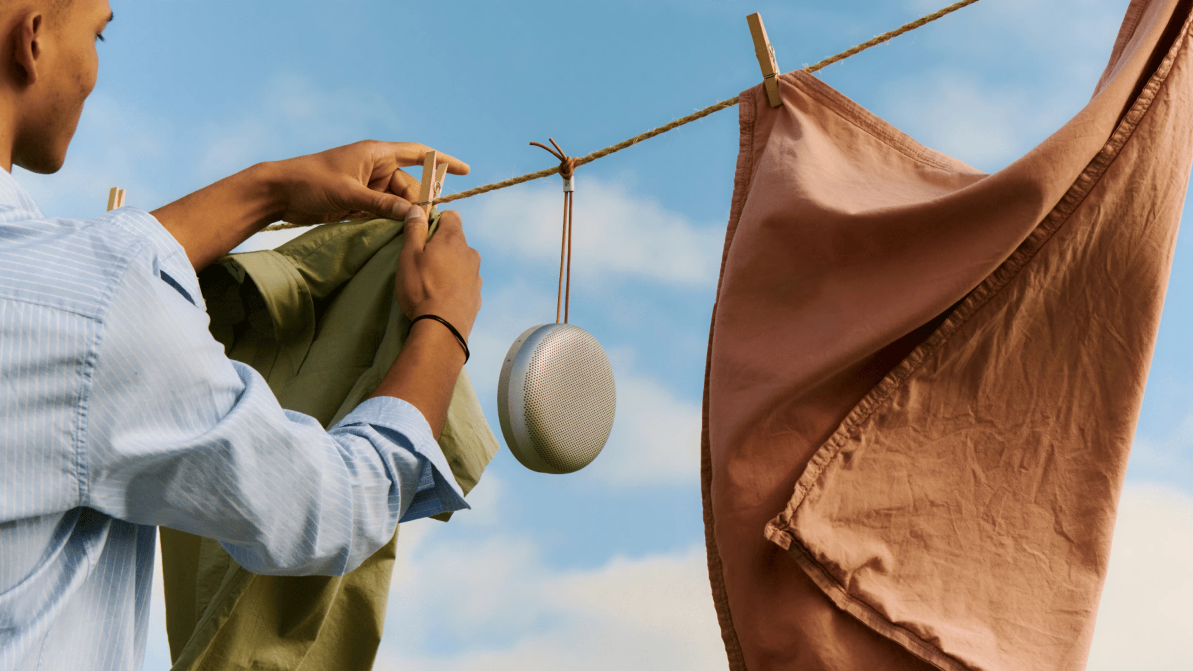 Person hanging laundry with the Beosound A1 3rd Gen