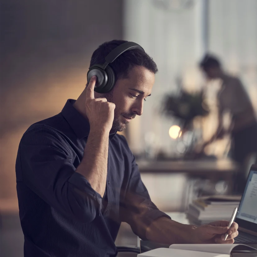 A man using Beoplay HX's touch interface to activate noise cancellation while working from home