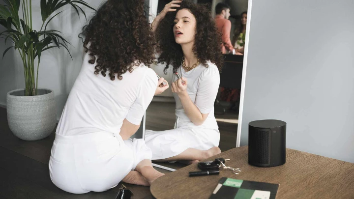 Beoplay M3 speakers on table next to girl putting make up on