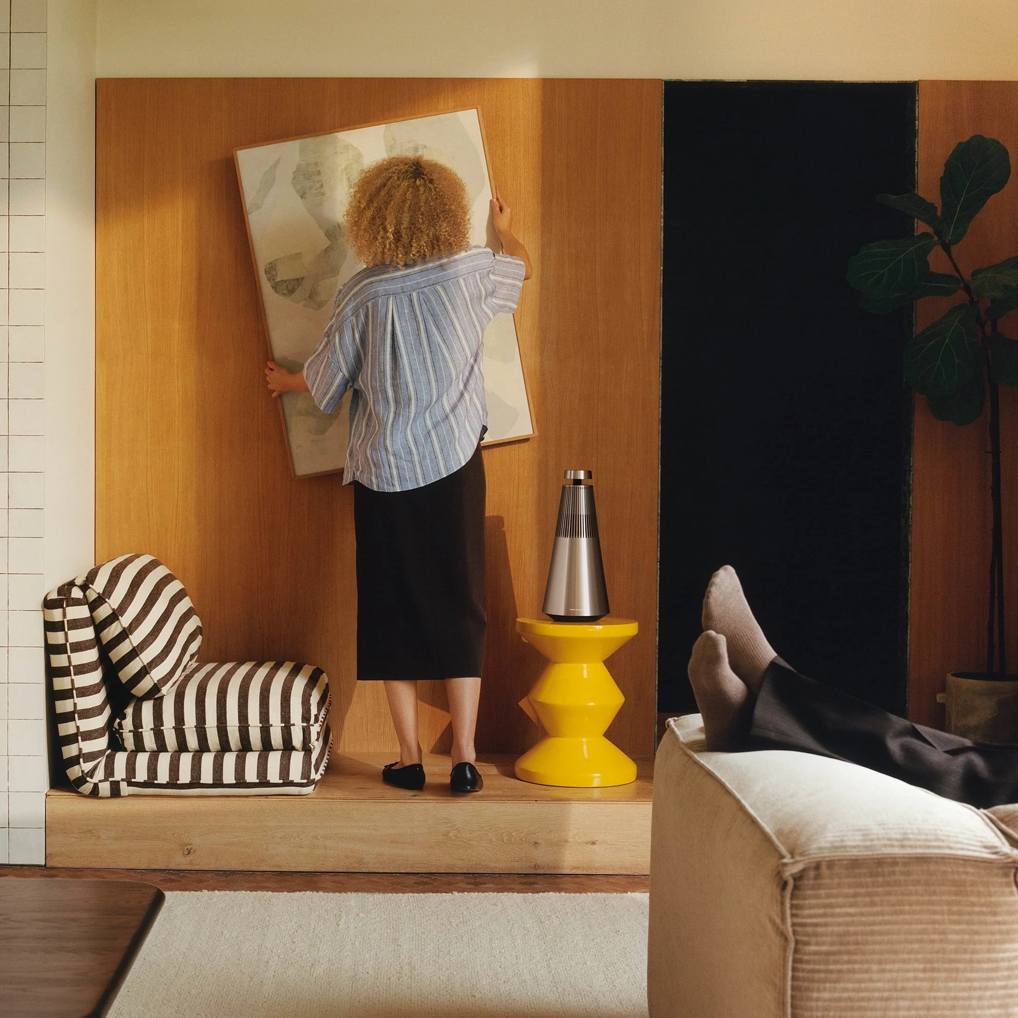 Person hanging up picture frame next to a Beosound 2