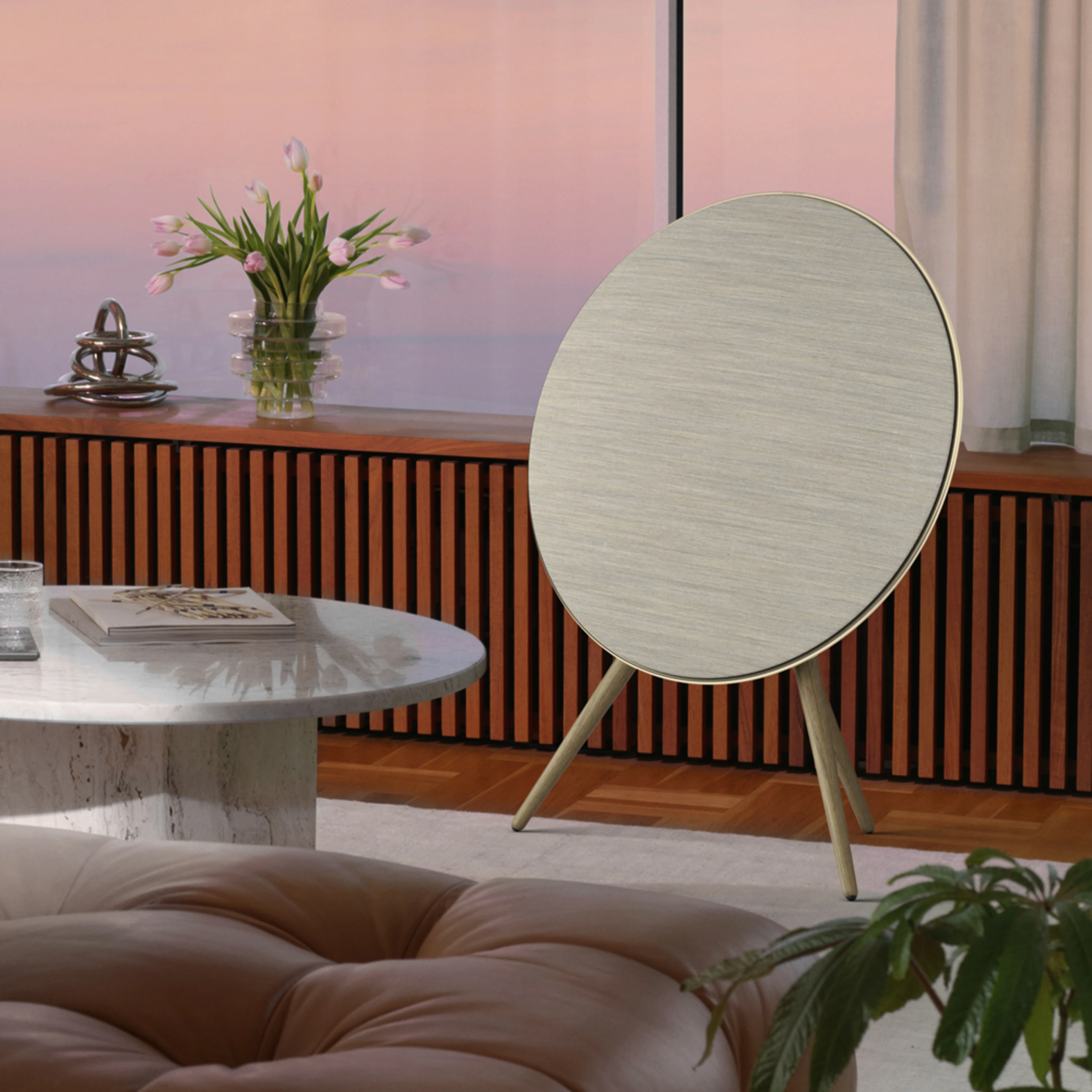 Beosound A9 speaker in Gold Tone with a grey fabric cover in a living room setting.