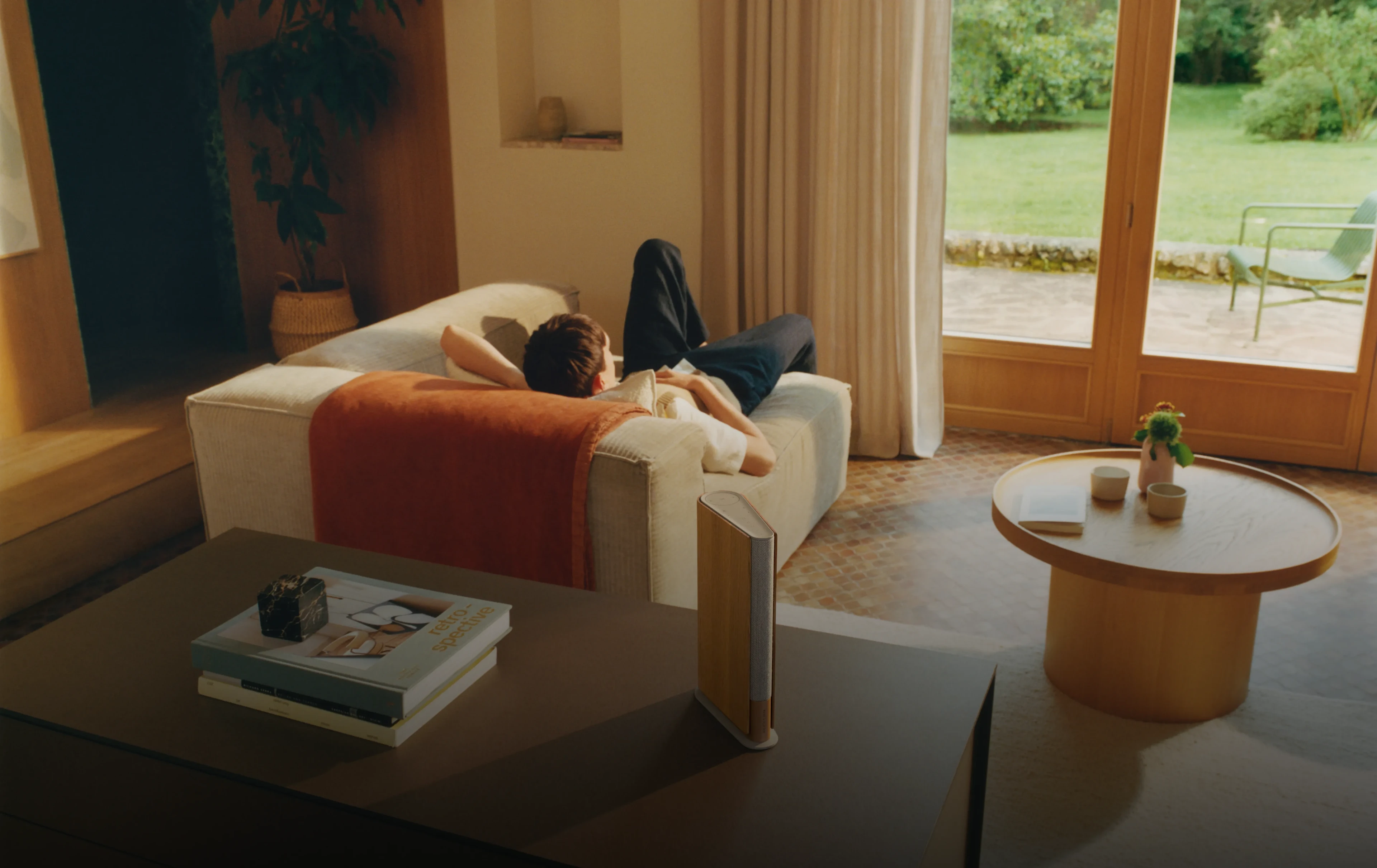 Beosound Emerge on a shelf in a living room where a person is lying on a sofa.
