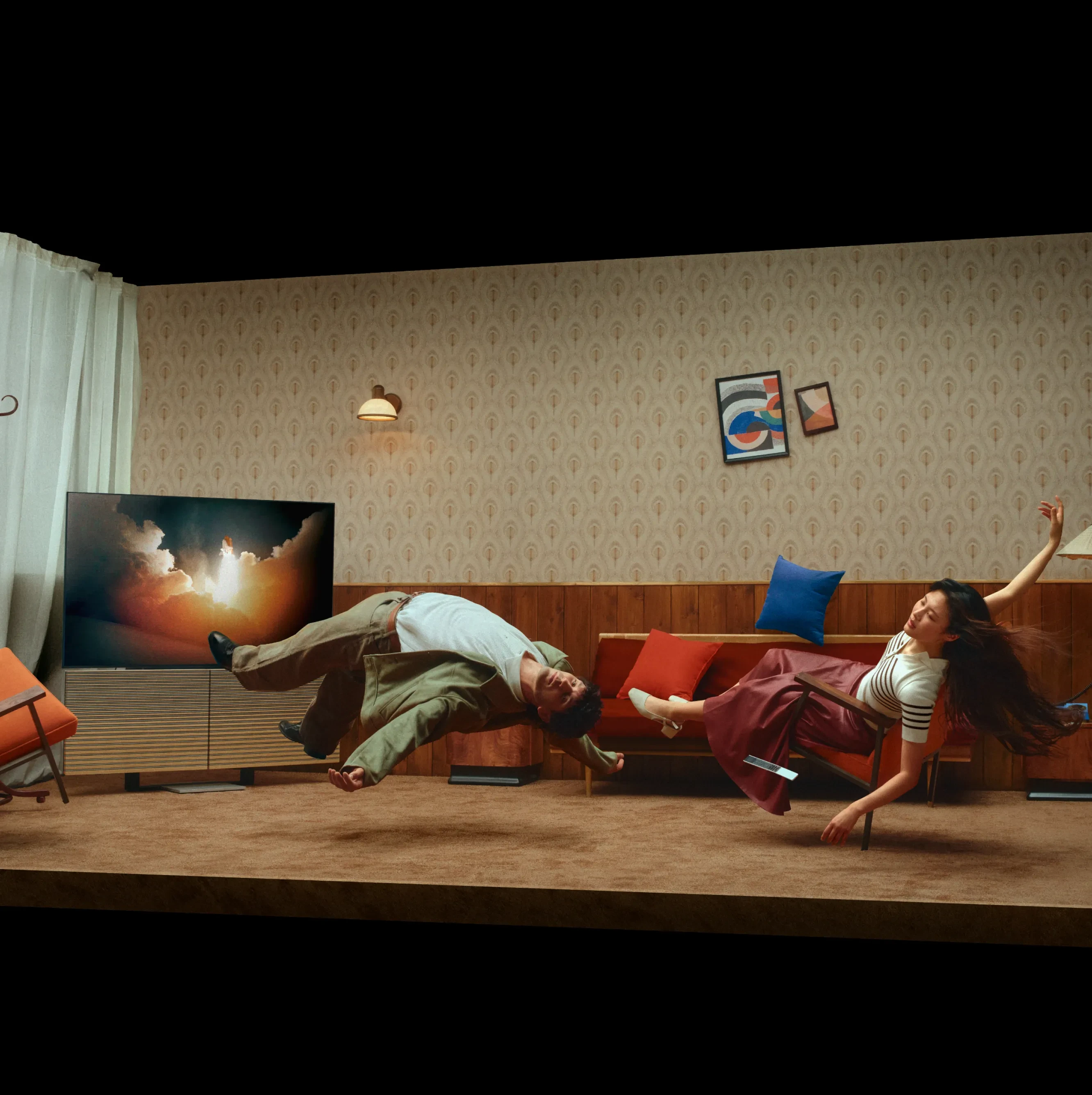 Two people floating sideways in a retro living room with patterned wallpaper, colorful cushions, and abstract art on the wall.