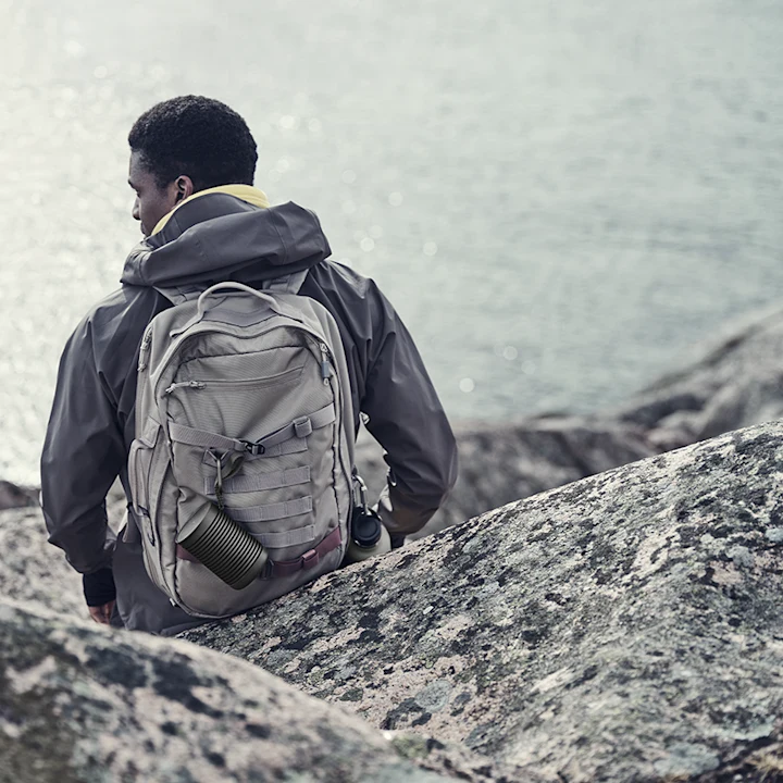 A person carrying Beosound Explore outdoor speaker while hiking
