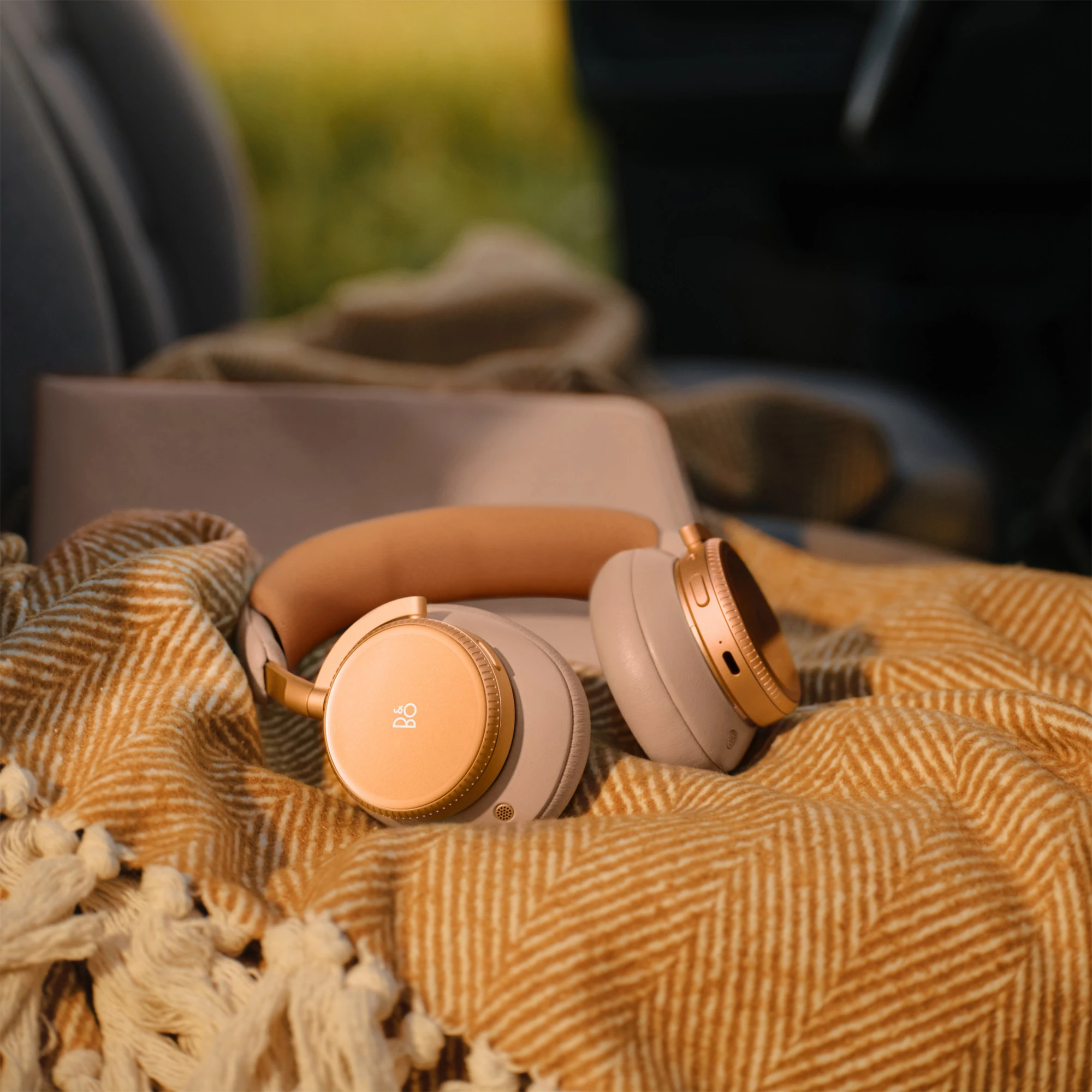 A pair of sunset apricot Beoplay H100 headphones on top of a blanket in a car