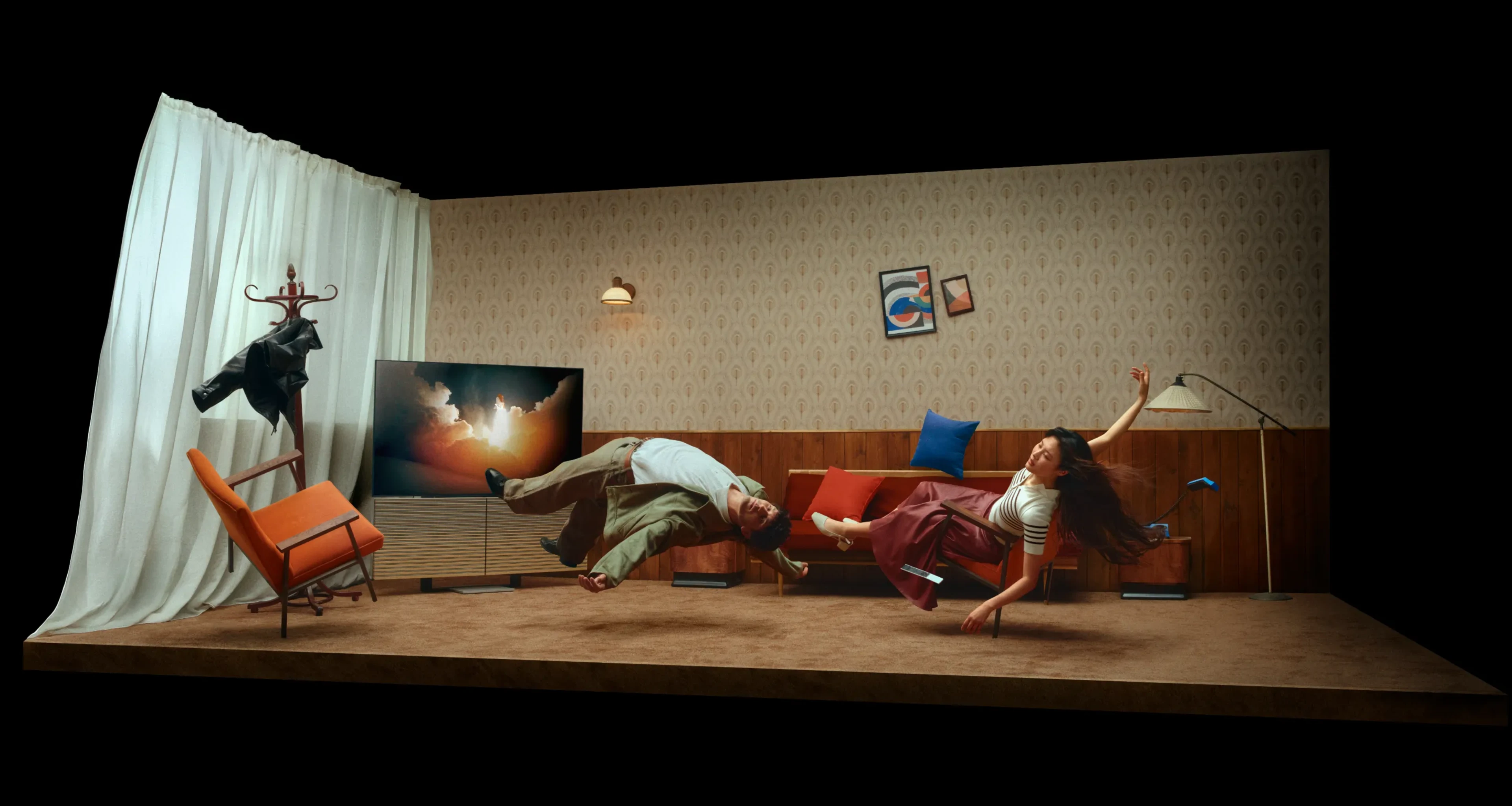 Two people floating sideways in a retro living room with patterned wallpaper, colorful cushions, and abstract art on the wall.