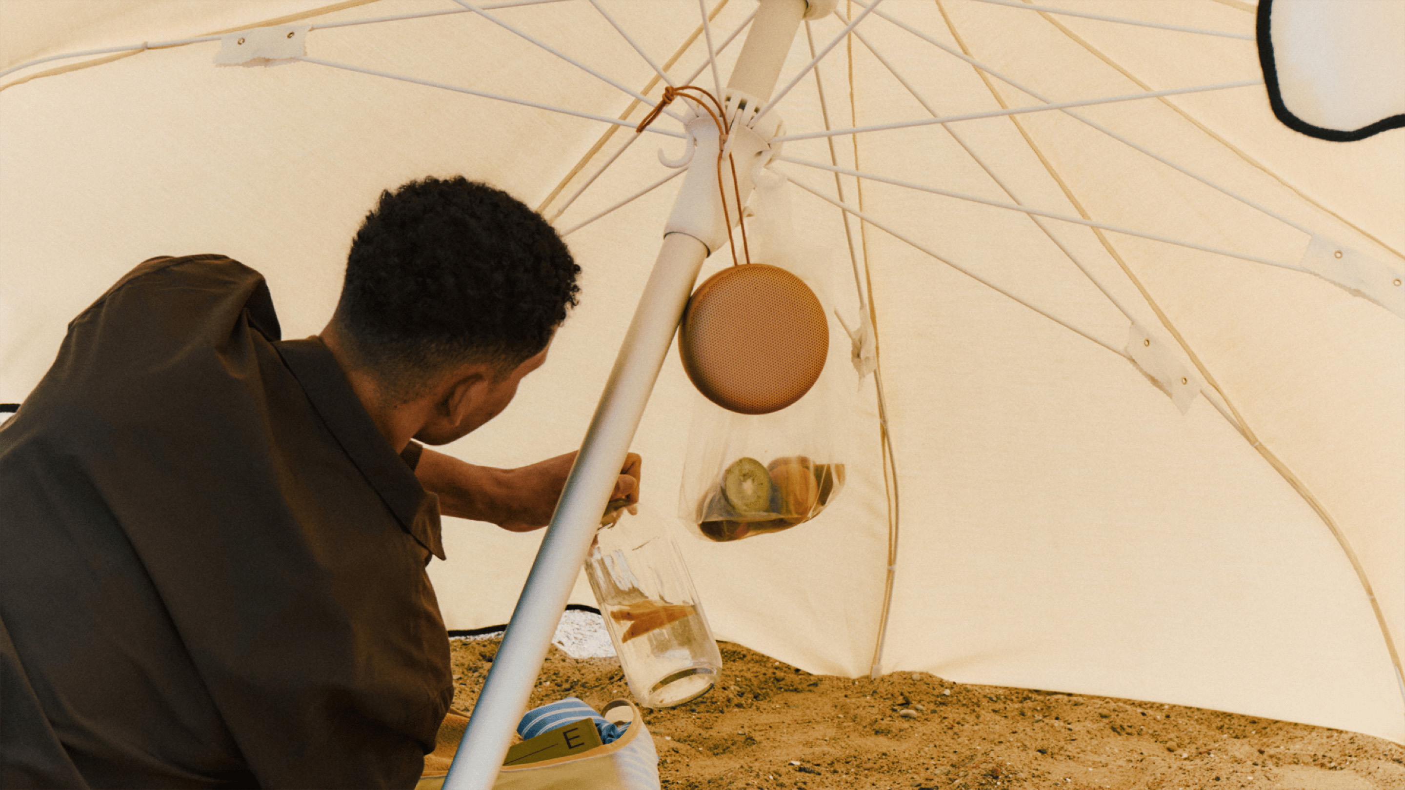 Person sitting under an umbrella with the Beosound A1 3rd Gen