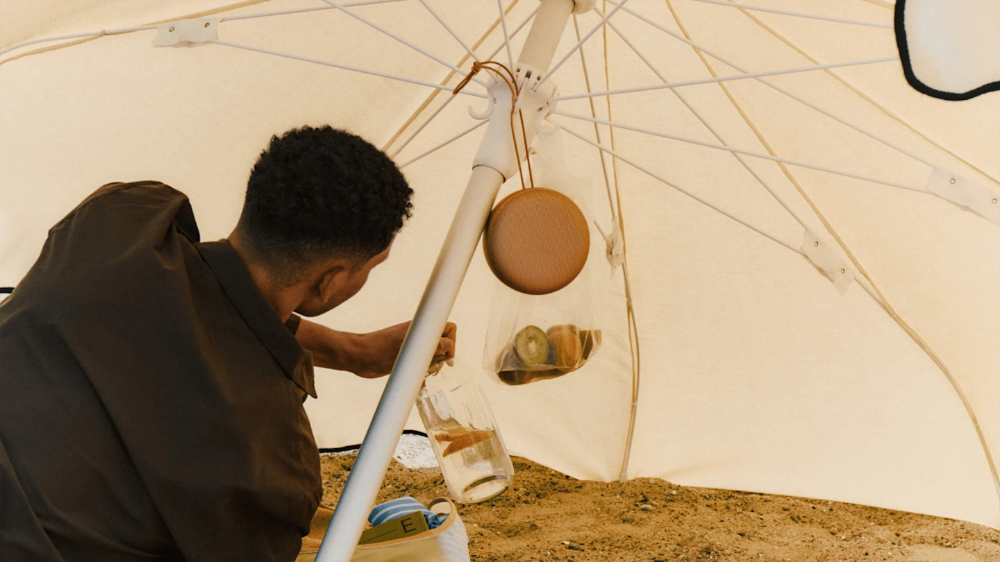 Person sitting under an umbrella with the Beosound A1 3rd Gen