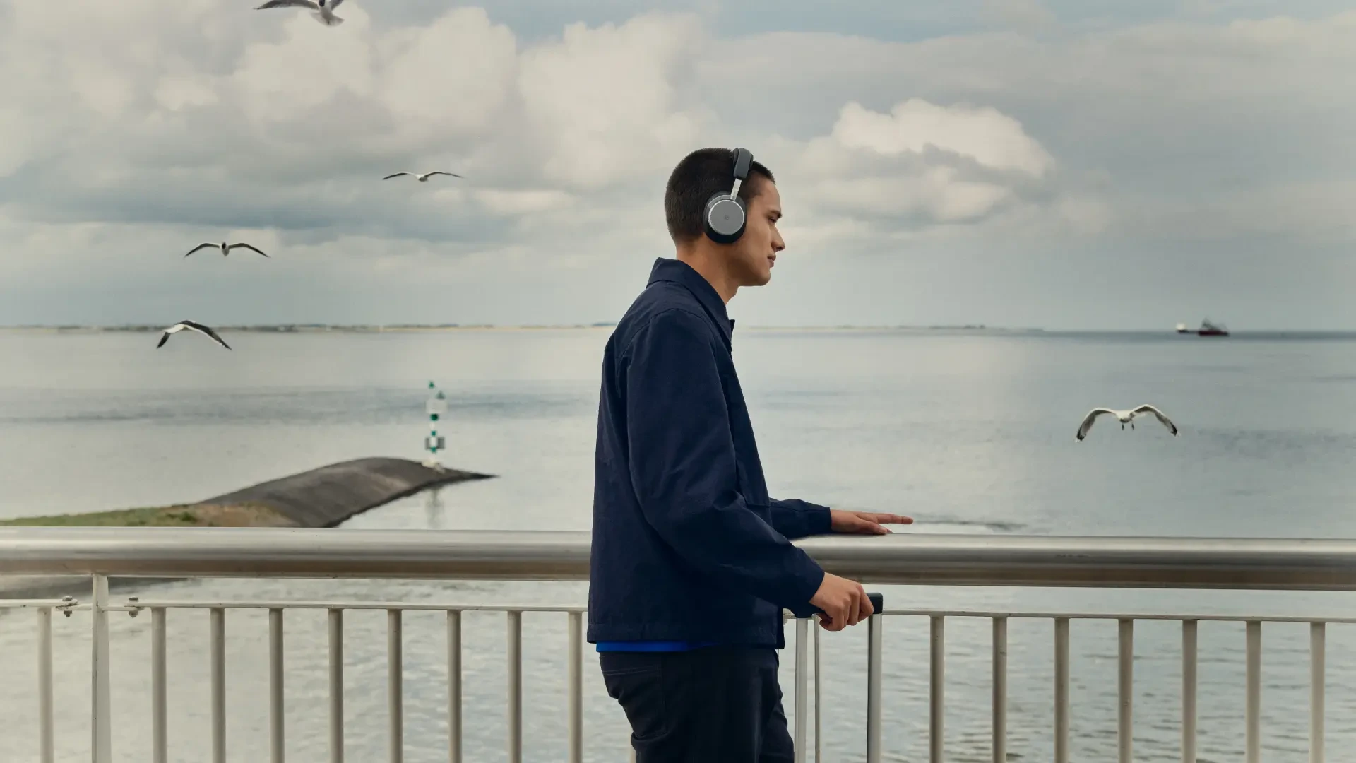 A man wearing Beoplay H100 standing by the sea