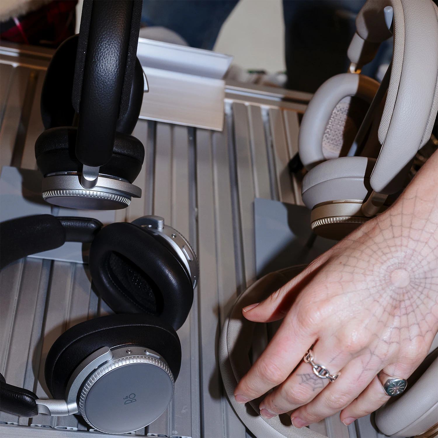 Four Beoplay H100s in Black and Sand, with a man's tattooed hand