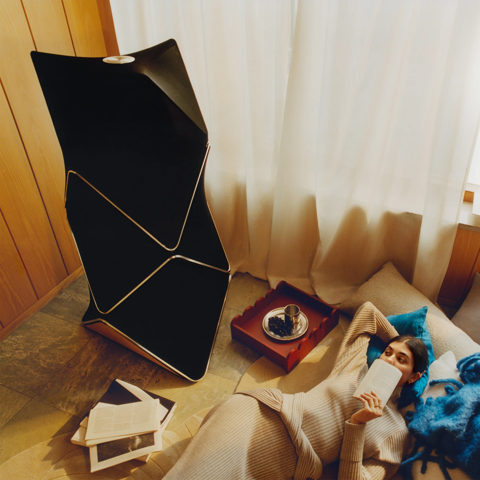 A woman lying on a couch next to a Beolab 90 speaker 