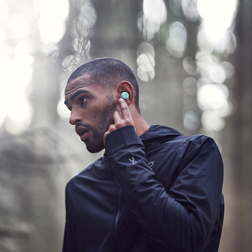 A man touching his left Beoplay E8 Sport earbud while running