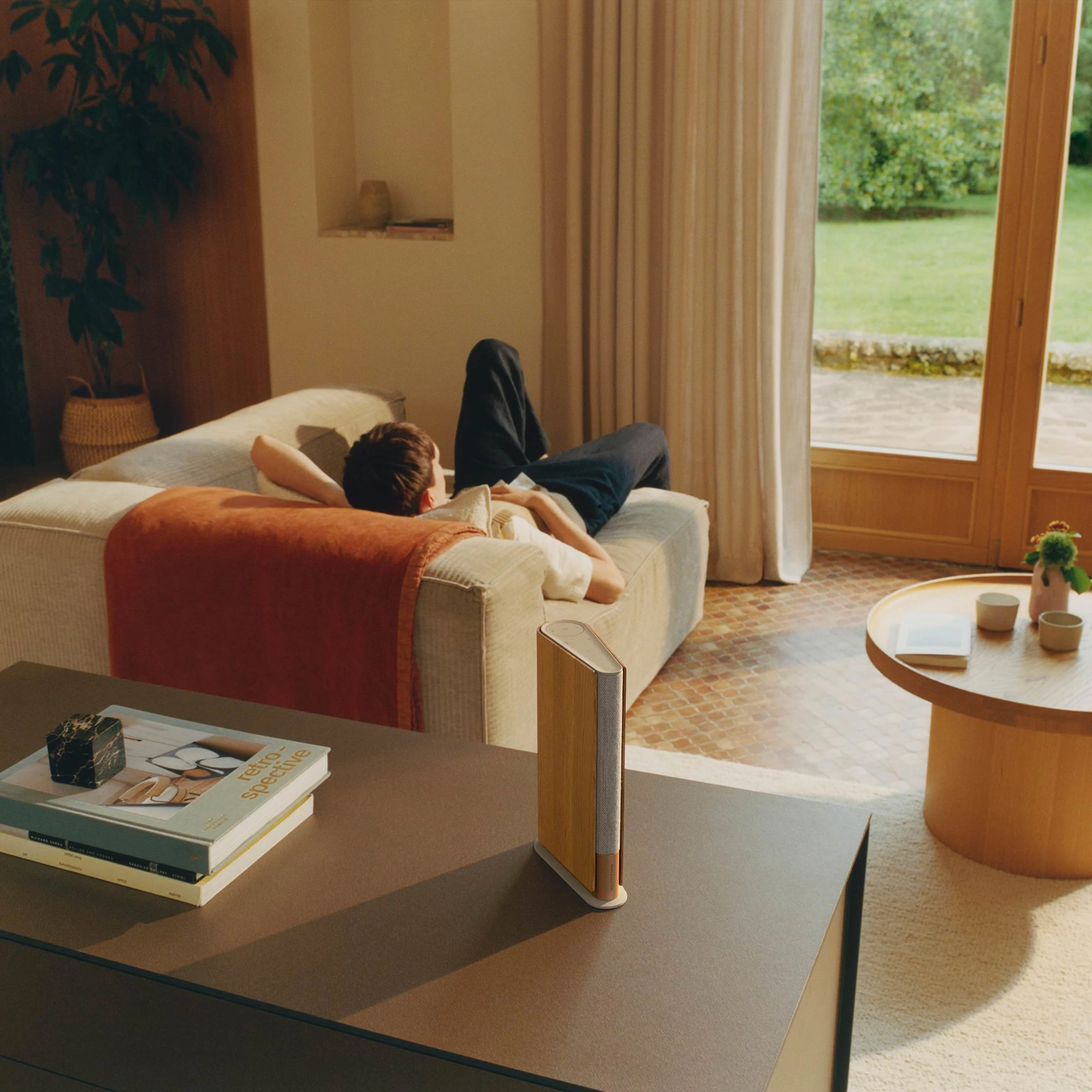 Person laying in a living on a couch were Beosound Emerge is placed on a table