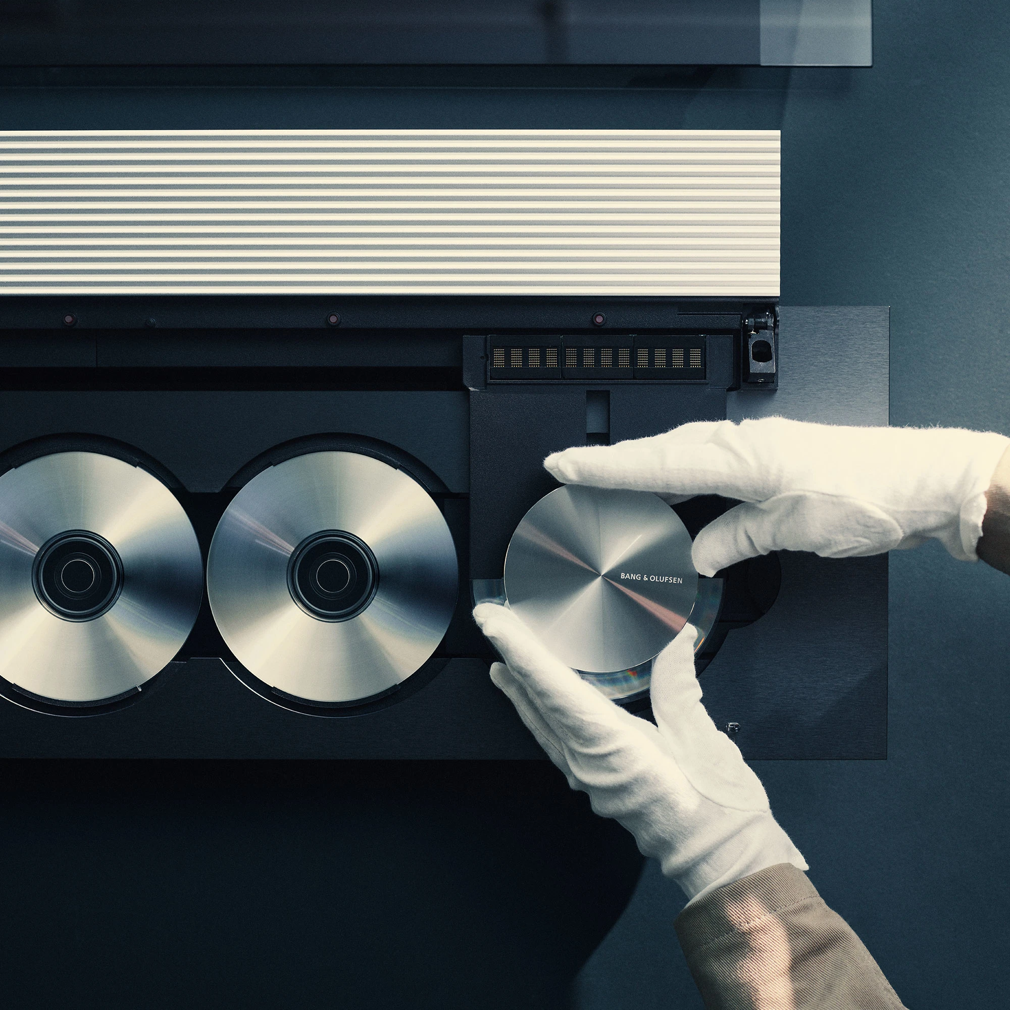 Detail image of a pair of hands in white gloves adjusting a Beosound 9000 CD player recreated as the Beosystem 9000c in Factory 3, Struer
