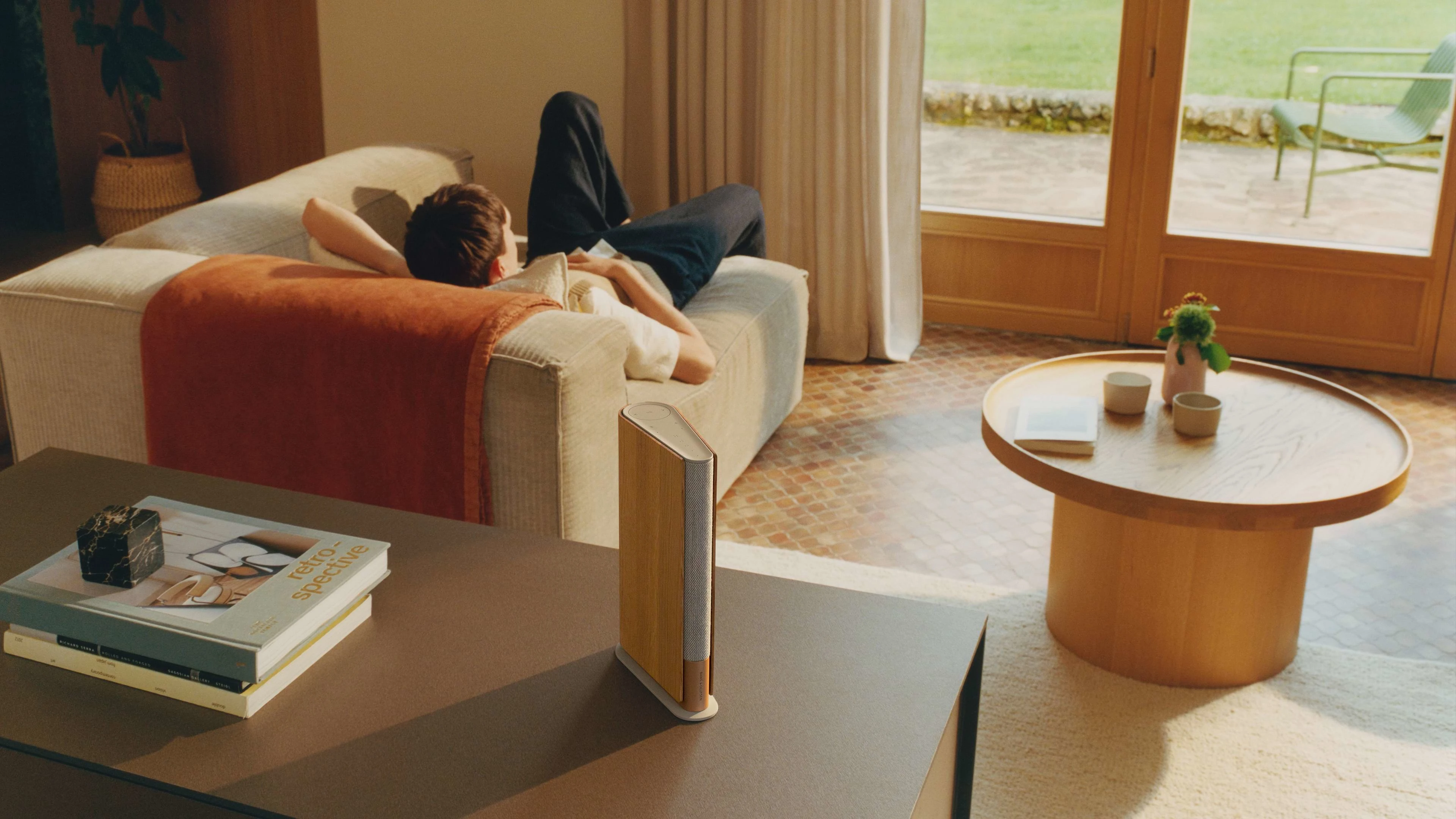 Beosound Emerge placed on a table with a person in the background on a couch