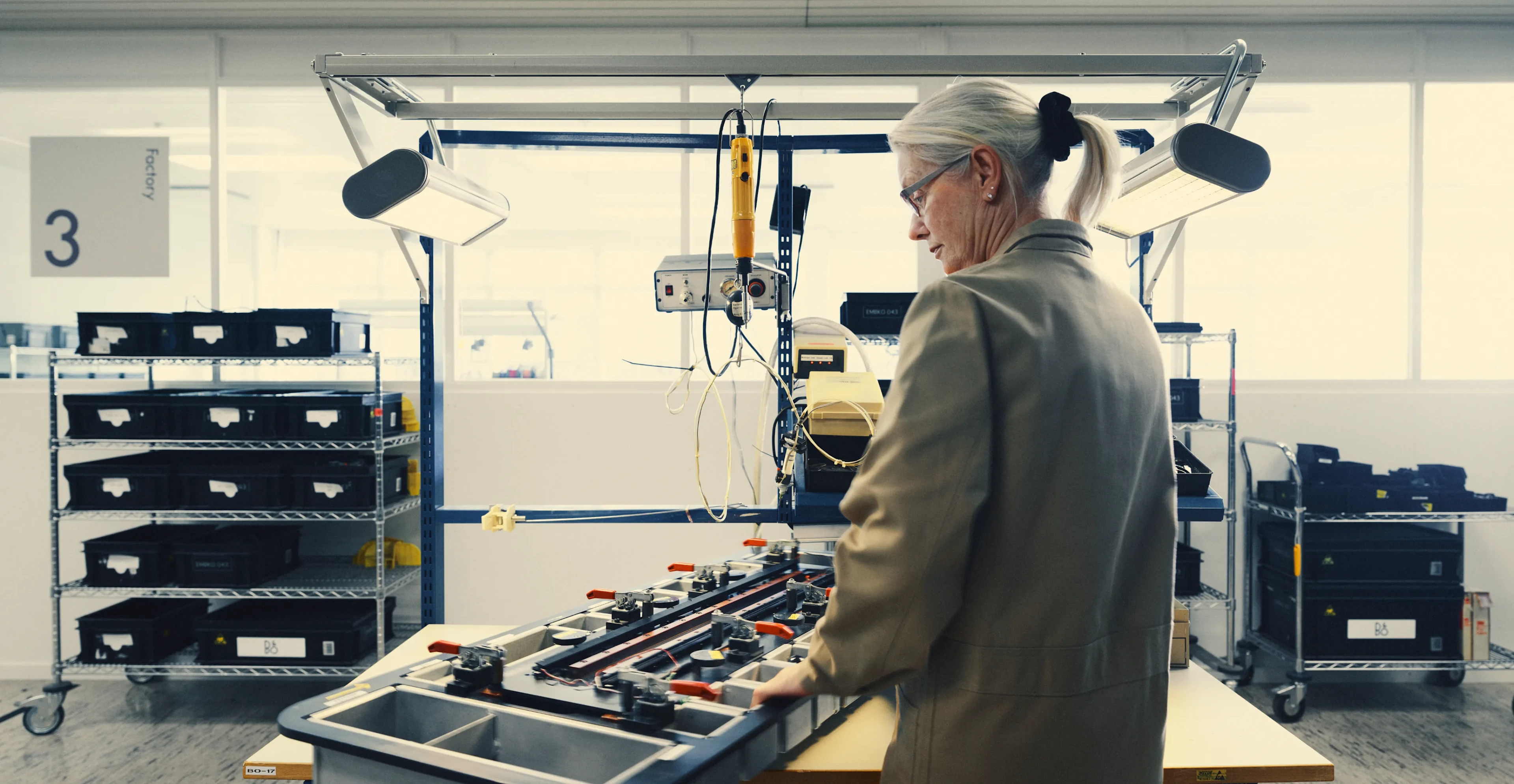 Person with gray hair working at an assembly station with technical equipment in a manufacturing facility.