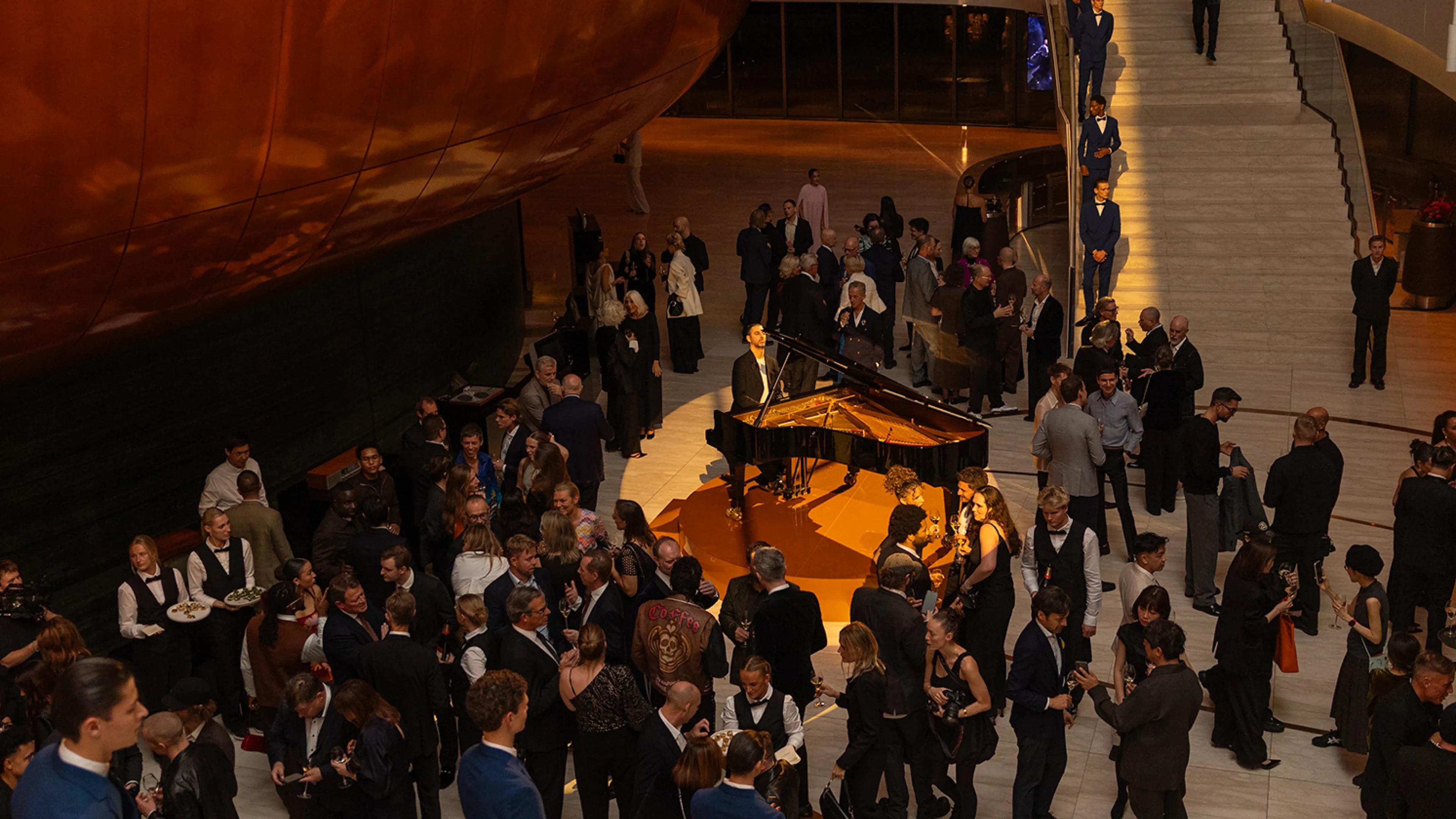 Pianist performing at grand piano in elegant venue with formally dressed guests gathered around during evening reception.