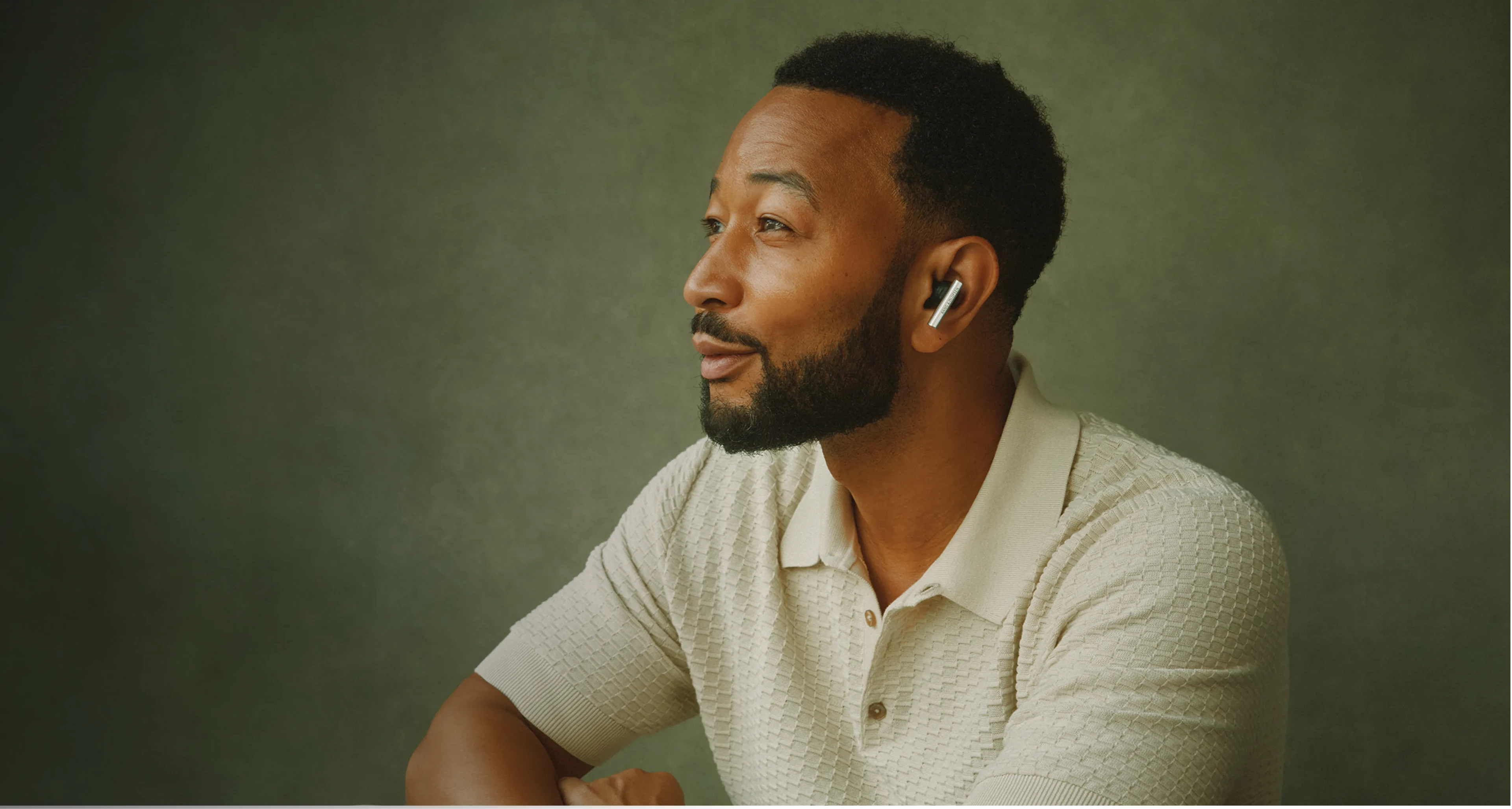 John Legend wearing a cream knit polo shirt and Beograce gazes thoughtfully to the side against a muted green background.