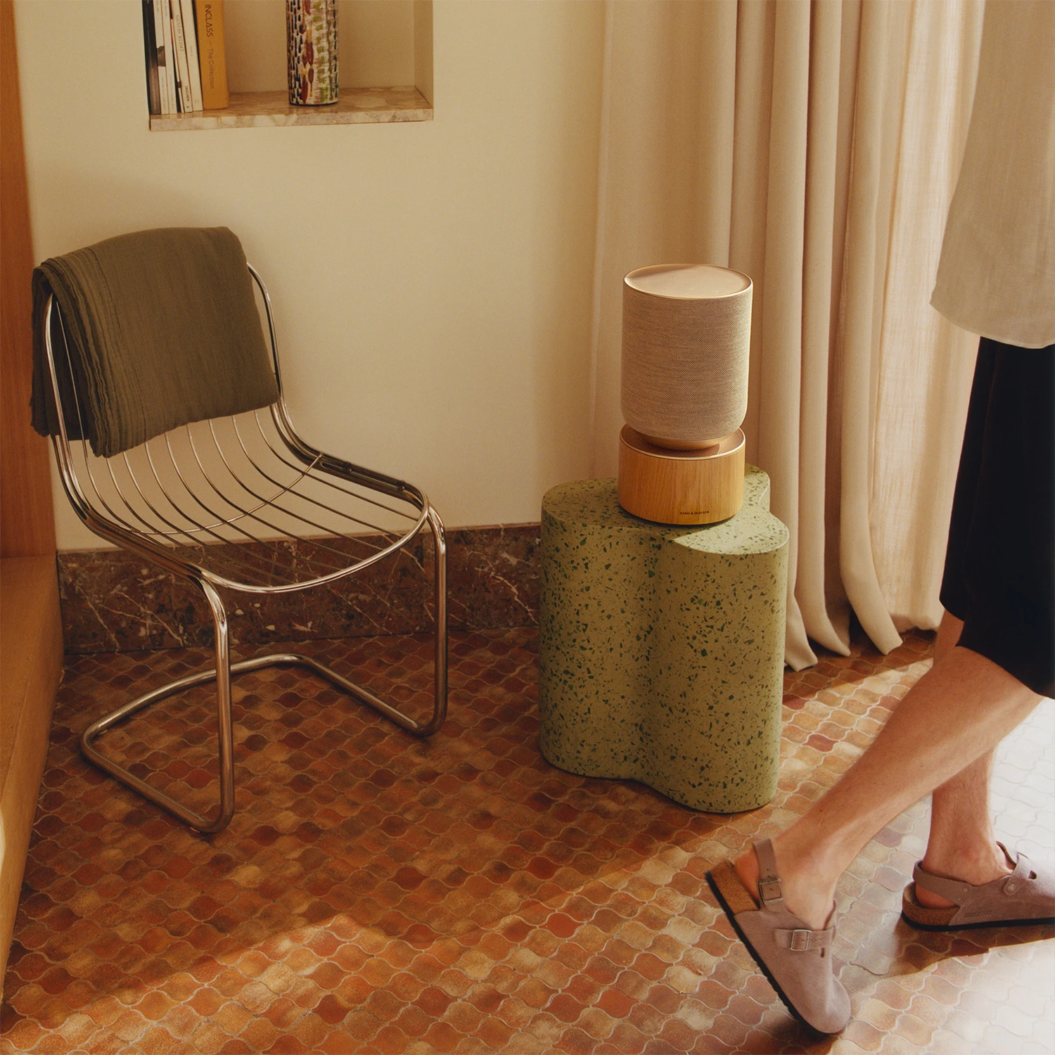 Beosound Balance on a stool next to a chair and a man walking by