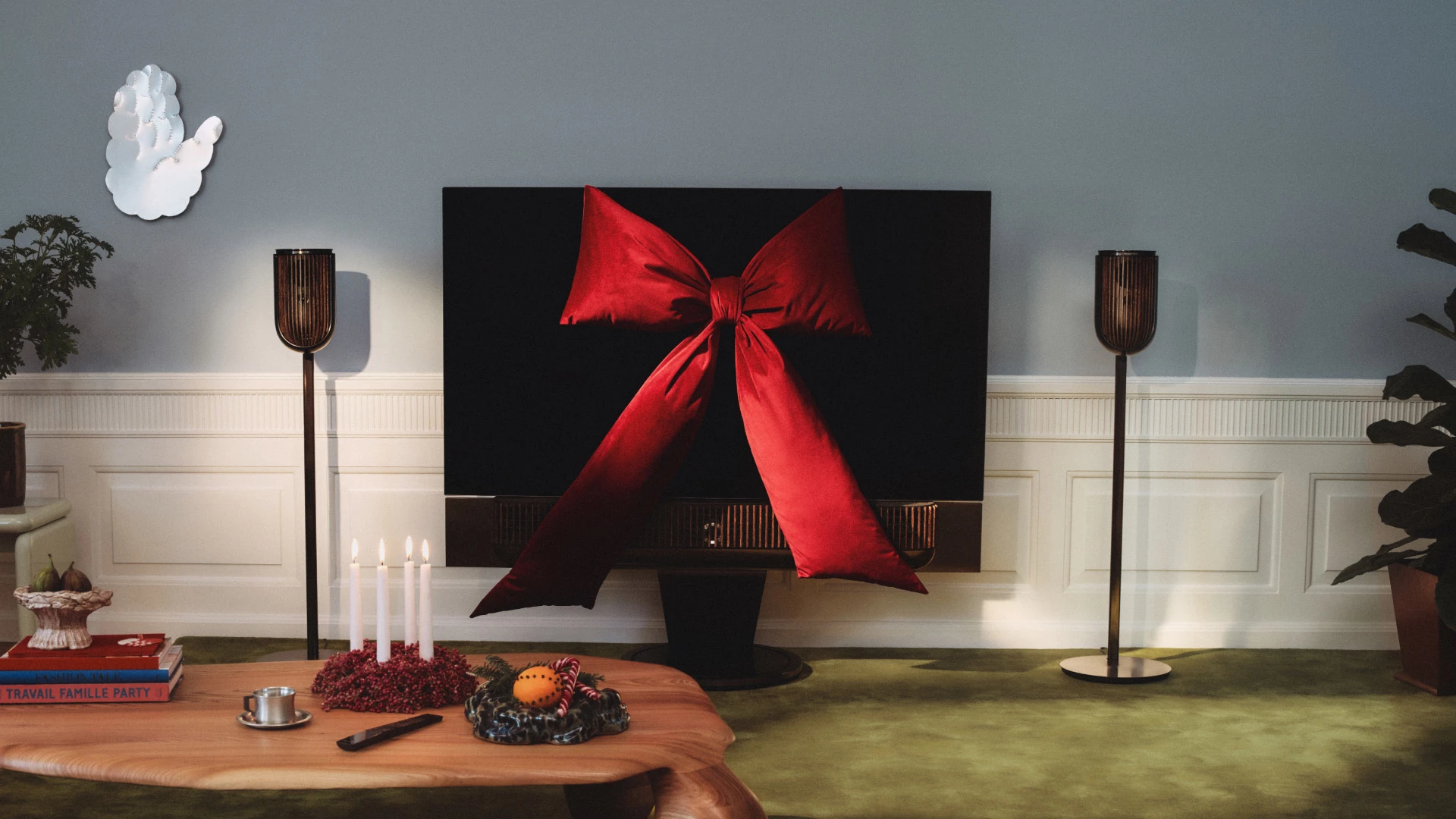 Beovision Theatre TV decorated with large red bow, wooden coffee table with candles and holiday decorations, floor lamp in cozy living room.