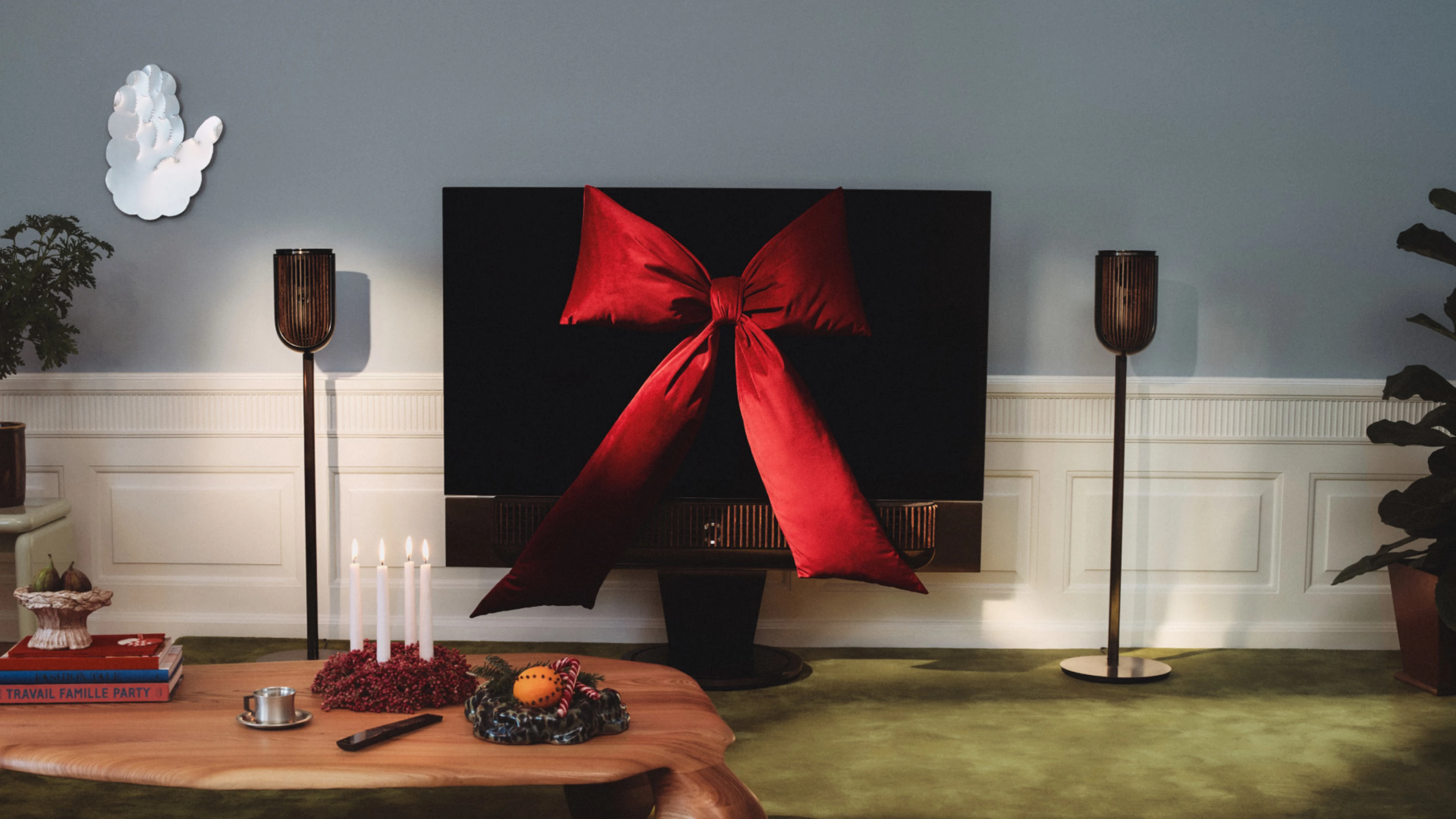 Beovision Theatre TV decorated with large red bow, wooden coffee table with candles and holiday decorations, floor lamp in cozy living room.