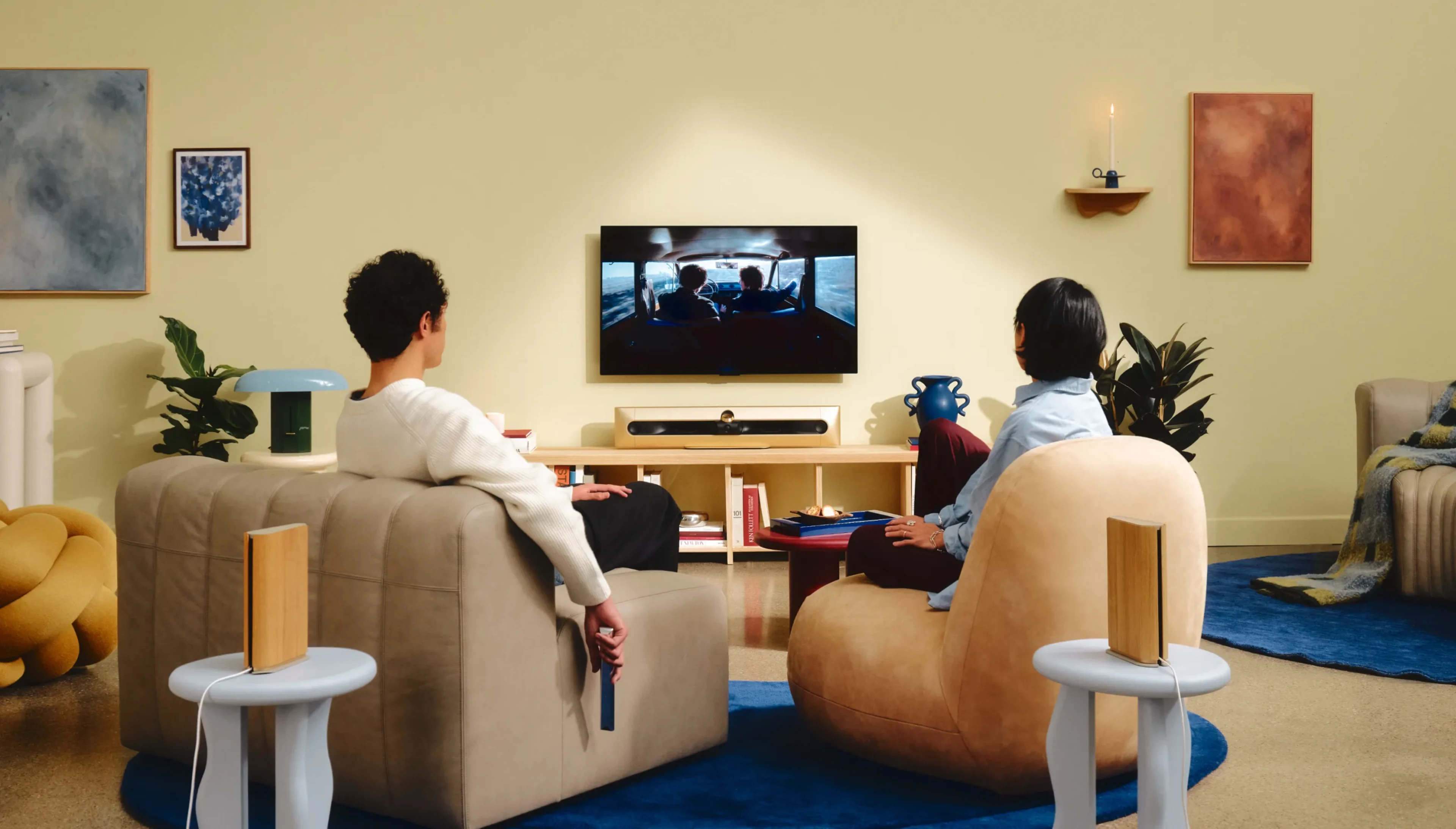 A couplesitting on a sofa in a modern interior living room watching TV, and there is a Beosound Premiere in Gold Tone variant under the TV