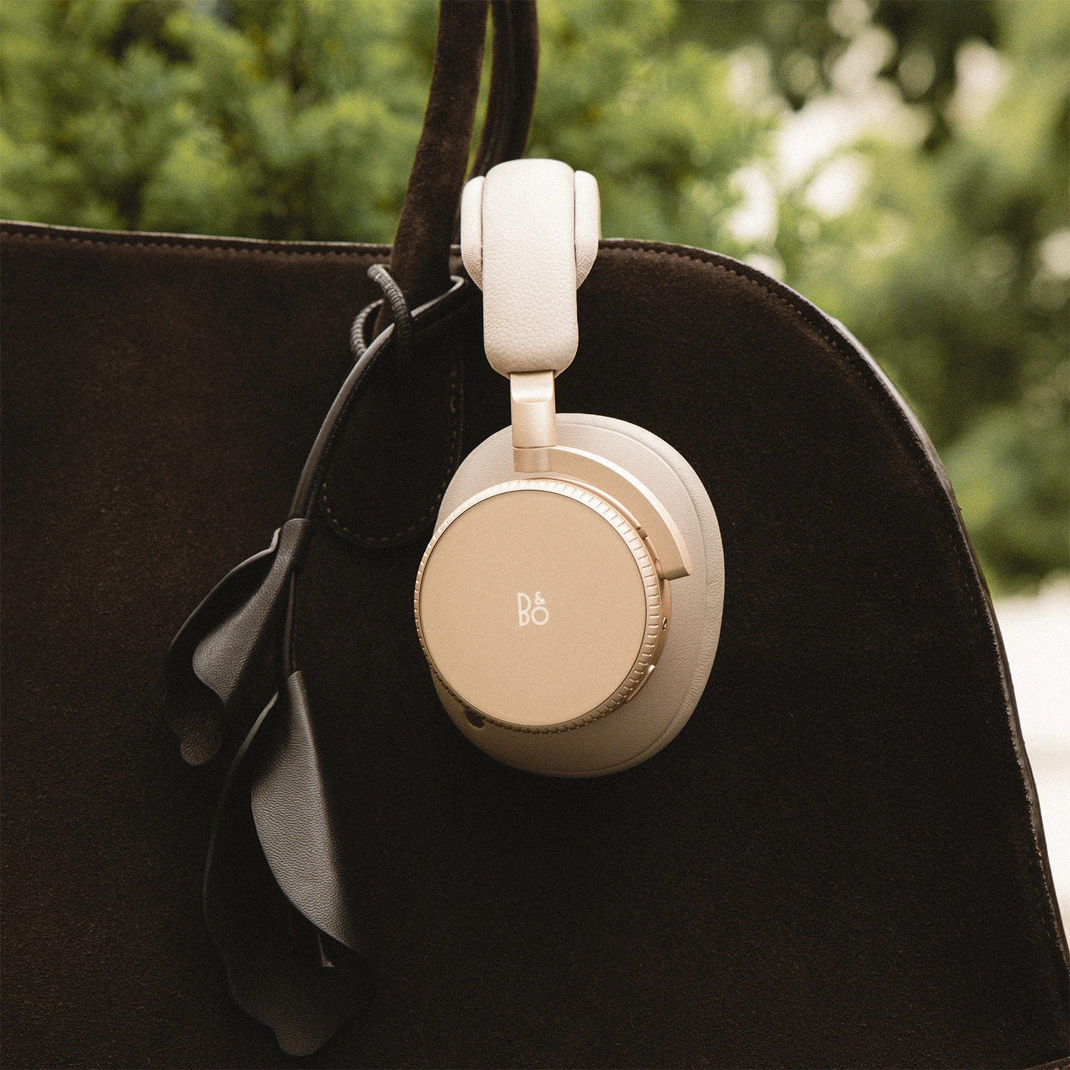 Beoplay H100 hanging from the side of a brown suede bag