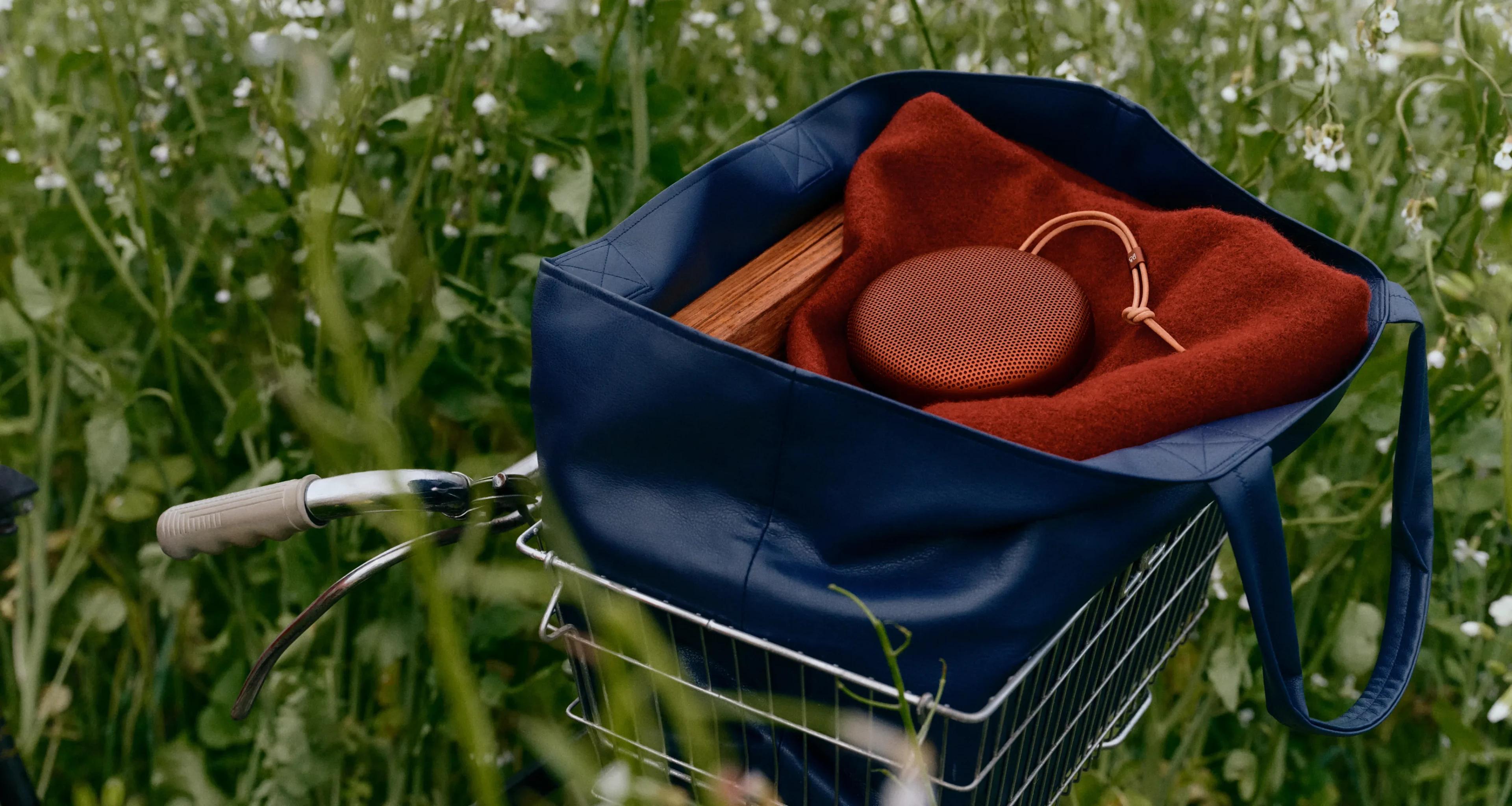 Beosound A1 Rustic Red ligger i en Dark Blue taske, der er placeret i en cykelkurv