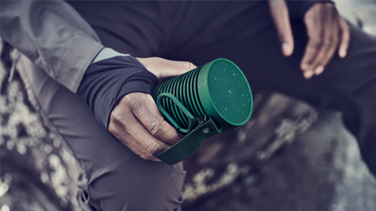 A man holds firmly Beosound Explore in green, before re-starting his hike